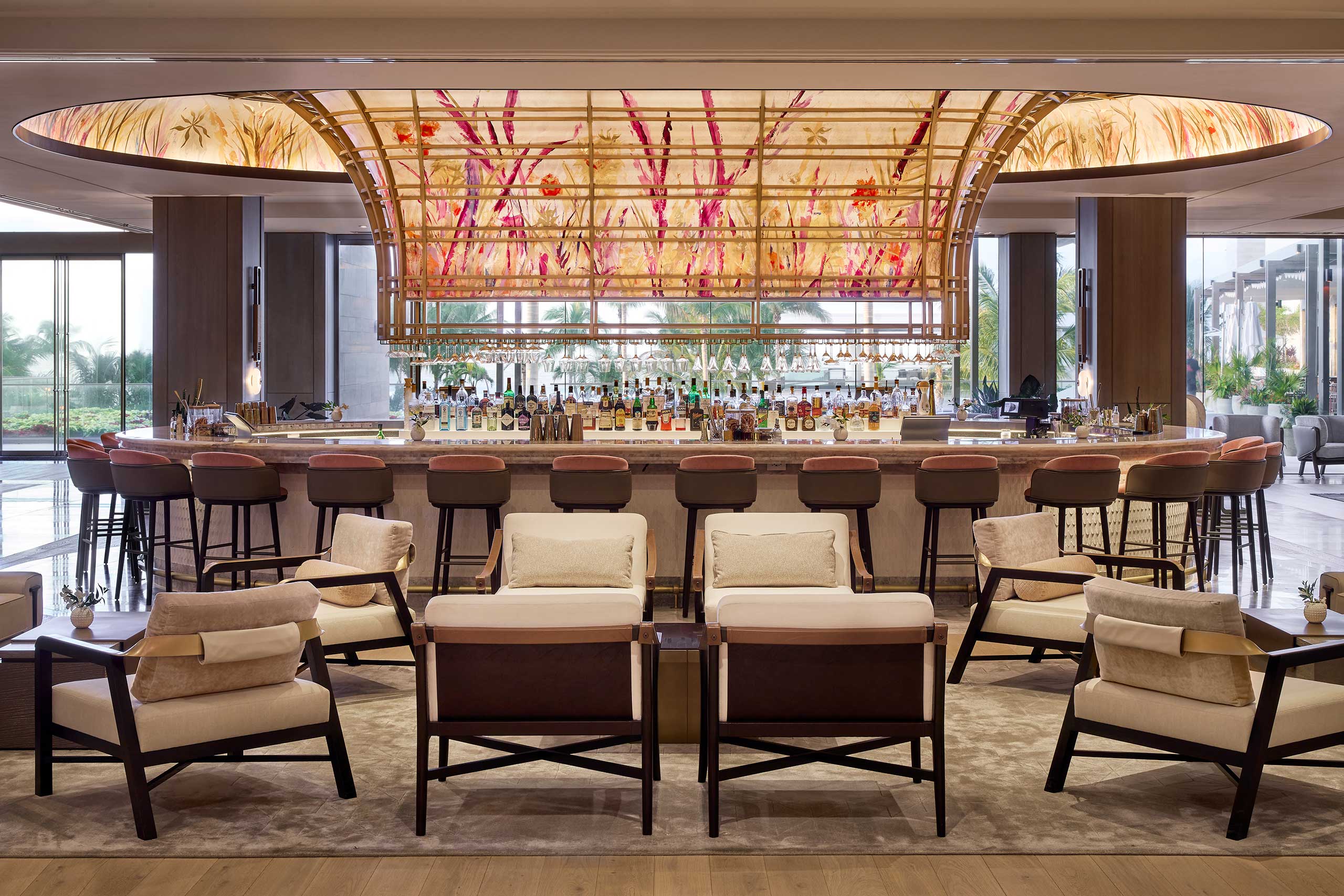 Luxurious hotel bar interior featuring a large, illuminated floral ceiling, surrounded by plush chairs and stools, creating a welcoming and elegant ambiance