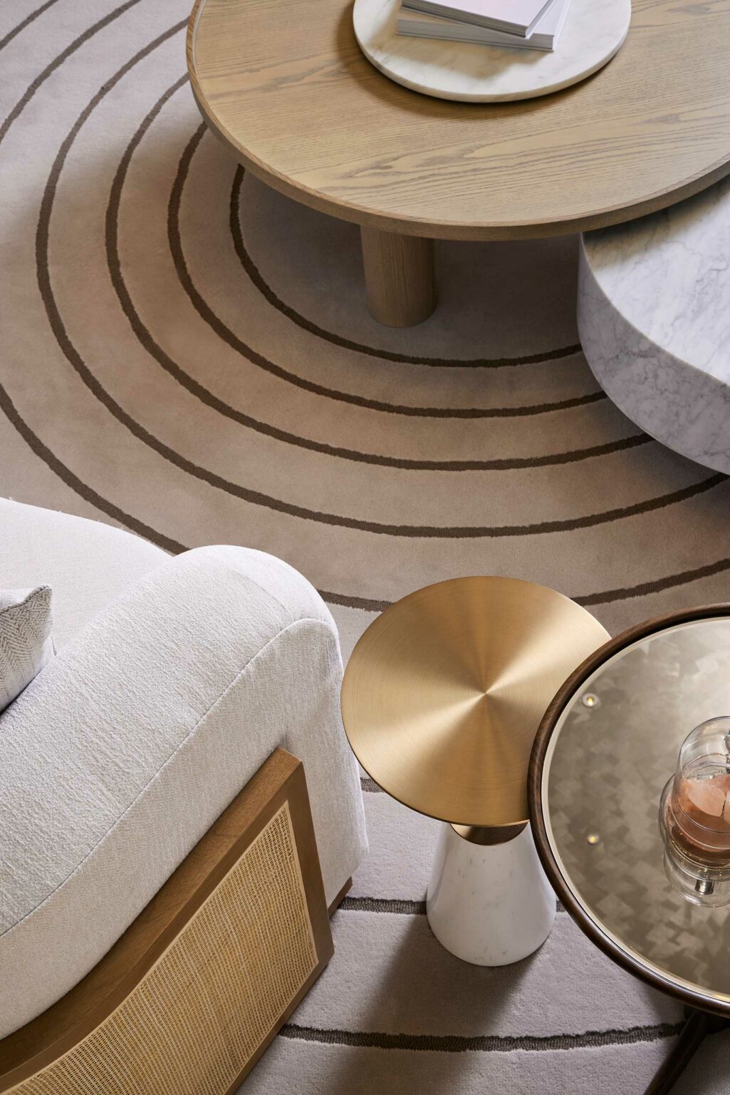Chic scene of a hotel lounge featuring a beige sofa, circular rug with brown concentric lines, tan wood and marble coffee tables, evoking a serene and modern ambiance.
