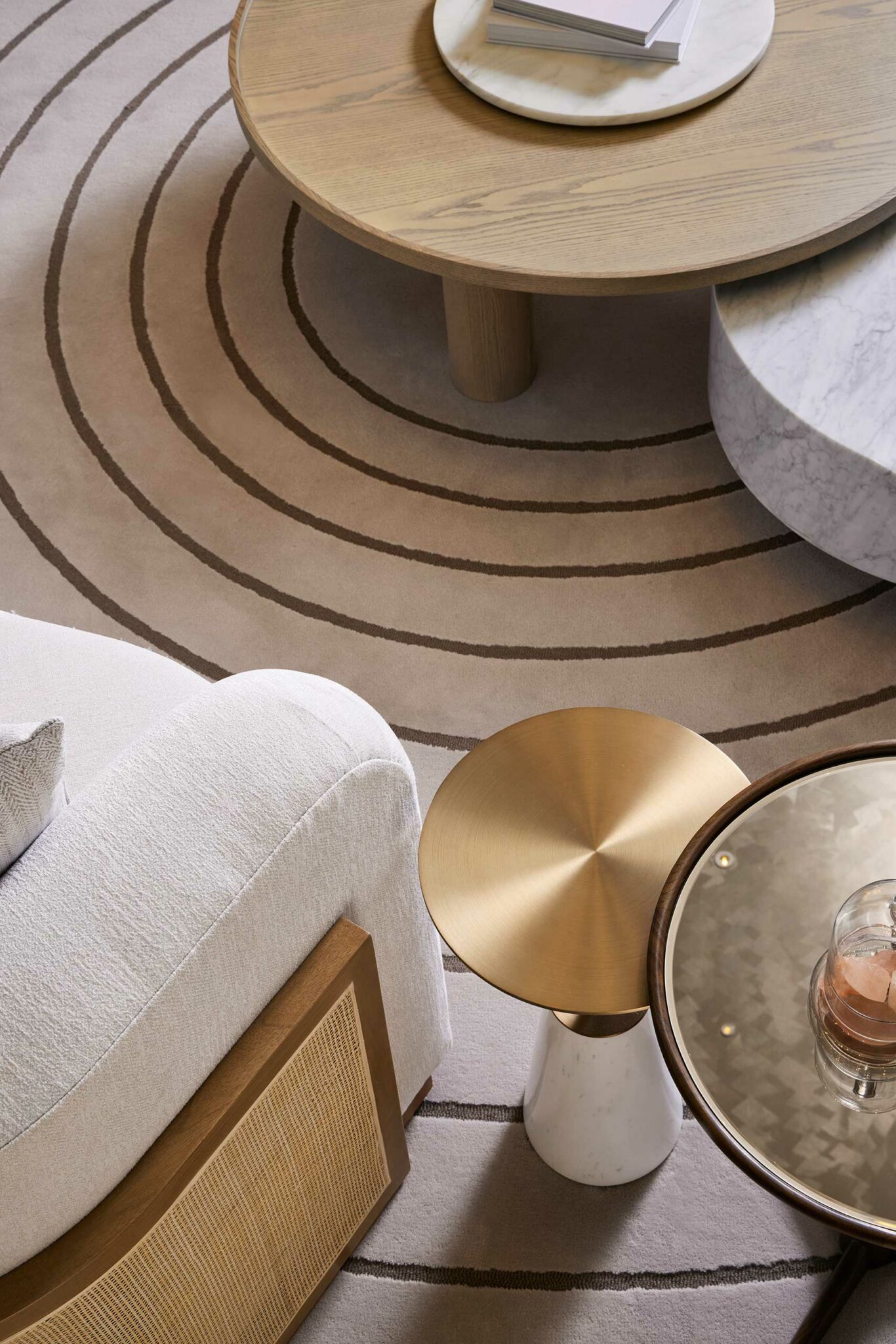 Chic scene of a hotel lounge featuring a beige sofa, circular rug with brown concentric lines, tan wood and marble coffee tables, evoking a serene and modern ambiance.