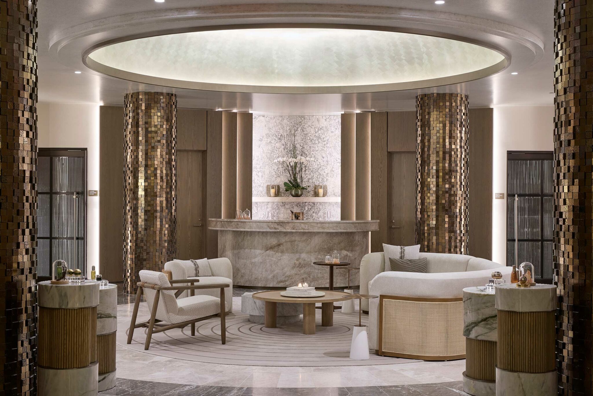 Elegant hotel lounge with neutral tones, featuring plush chairs, wooden tables, and gold accents. A marble reception desk and soft lighting create a luxurious ambiance.