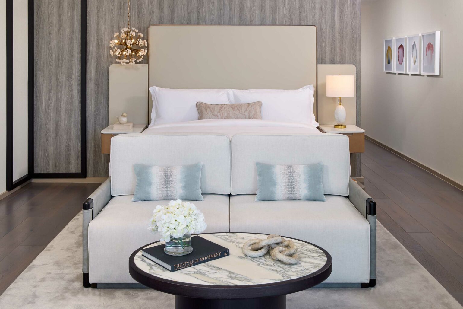Elegant suite bedroom with a large bed, two side tables with lamps, and a plush sofa. A small round table with a book and flowers adds a cozy touch.