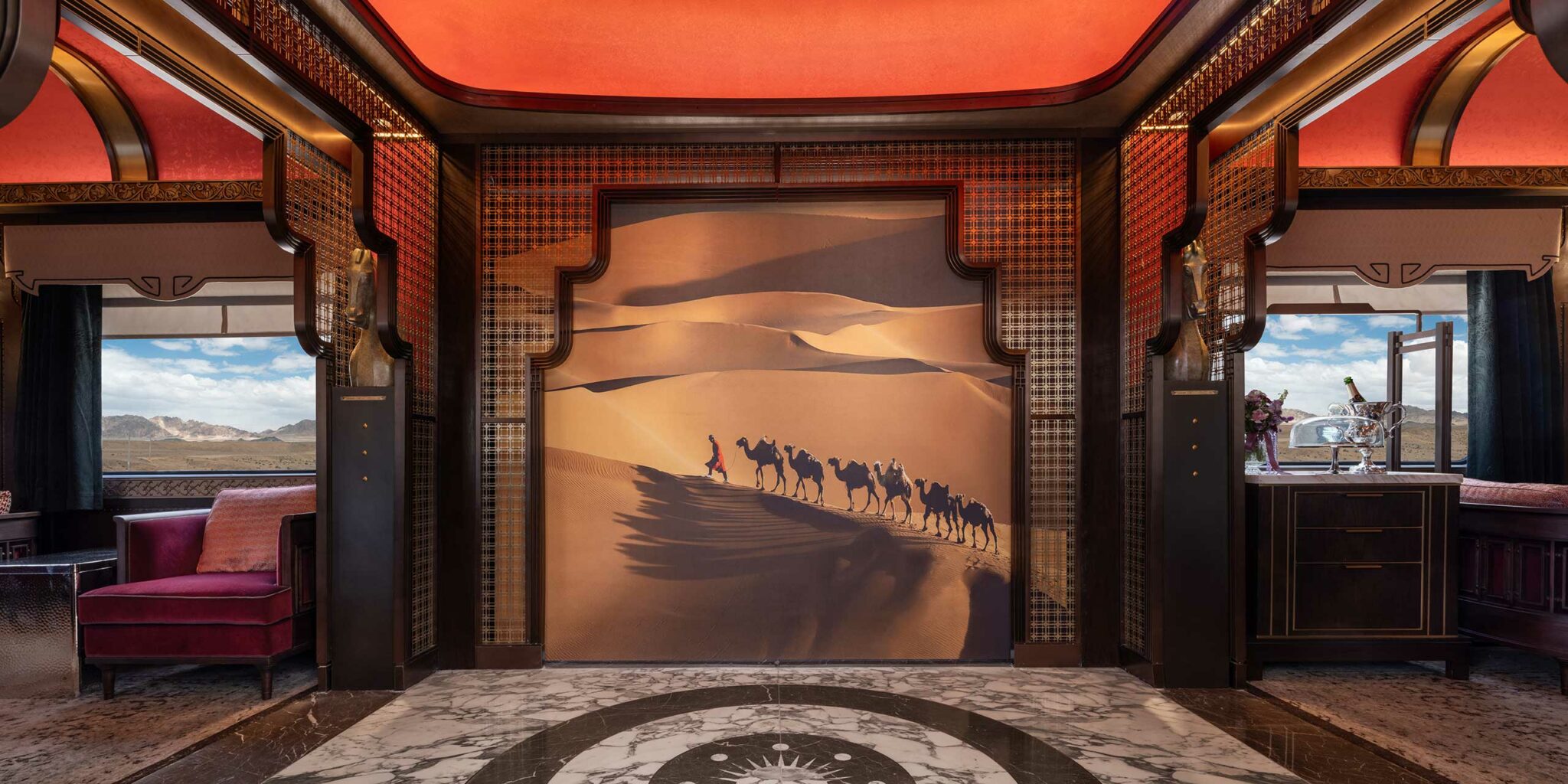 Luxurious train interior with an ornate design, featuring a central mural of camels in a desert. Warm red tones create an elegant and exotic ambiance.