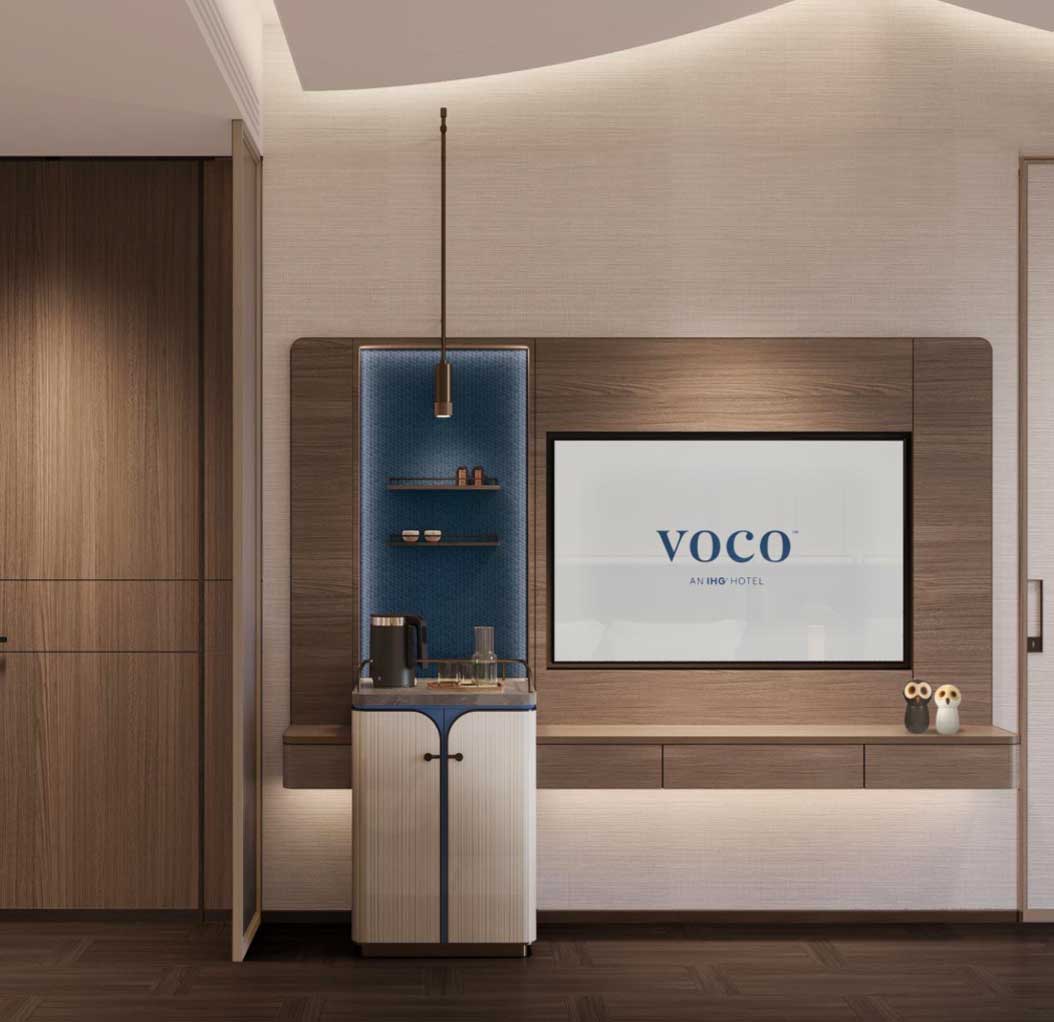 Modern hotel room with a stylish coffee station and shelves on the left. On the right, a large screen displays 