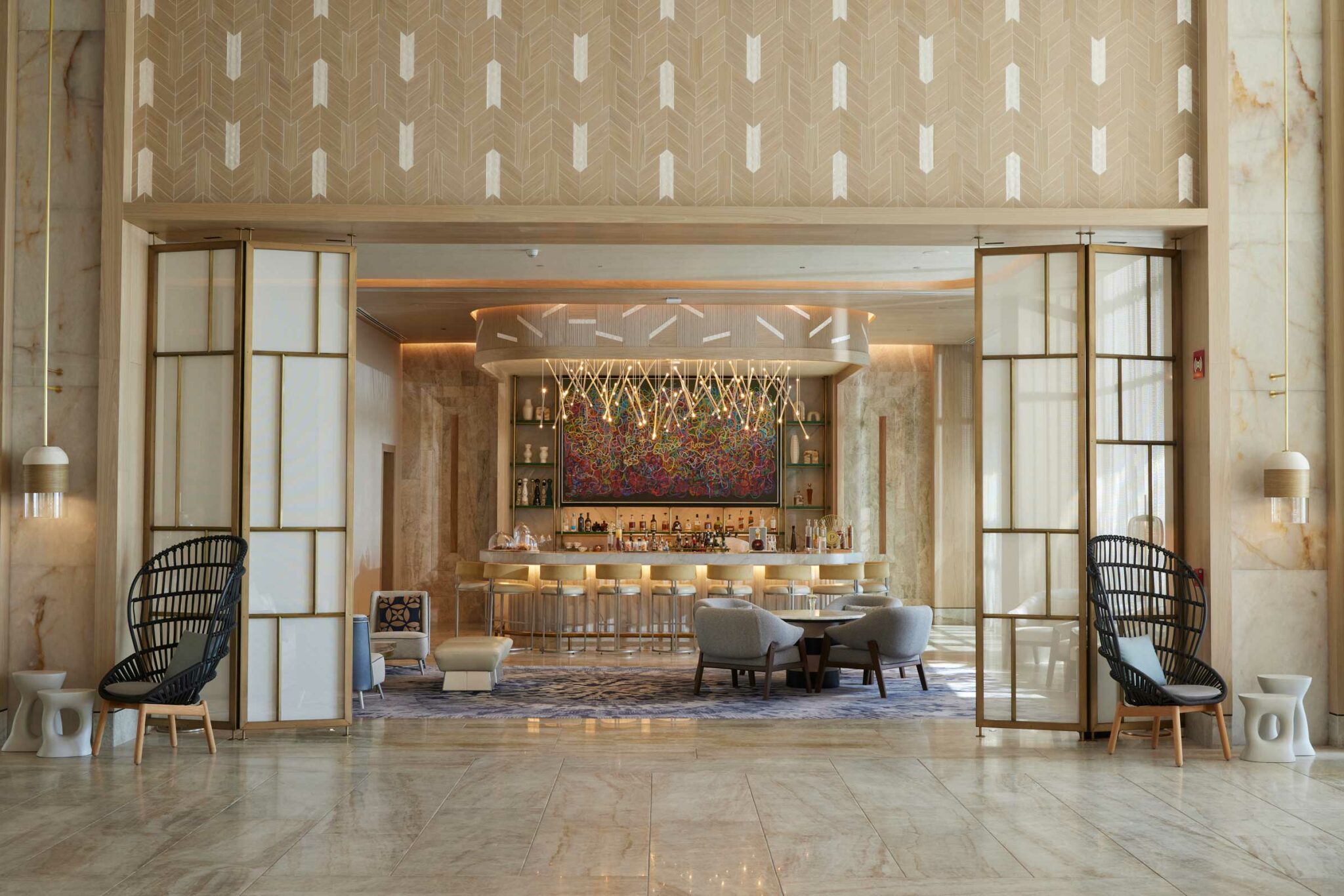 Elegant resort bar area with neutral tones, plush seating, and vibrant abstract artwork. Features modern chandeliers, creating a warm, inviting atmosphere.