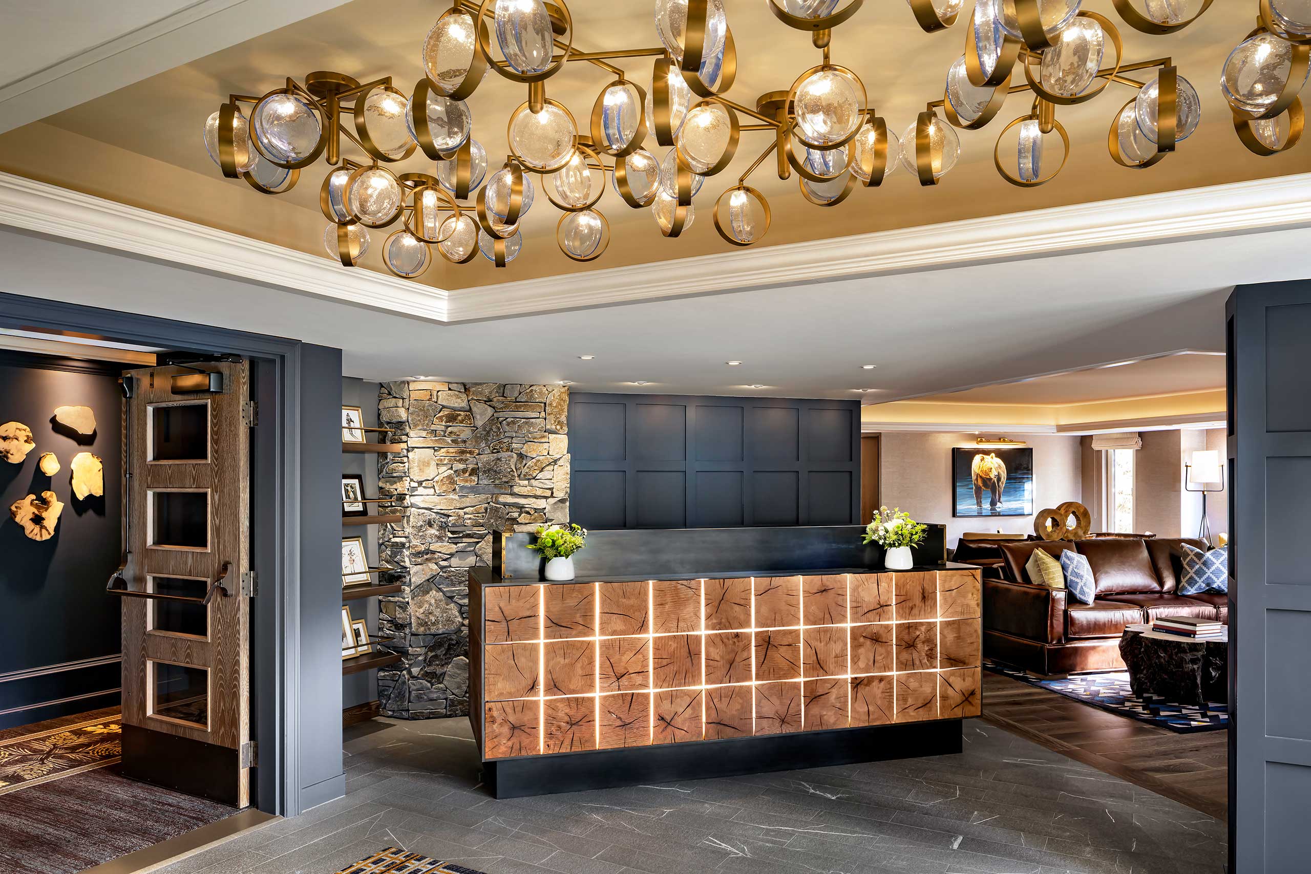 Luxurious hotel lobby with modern lighting, a wooden reception desk, stone accent wall, and cozy seating area featuring leather sofas, creating a warm, inviting atmosphere.