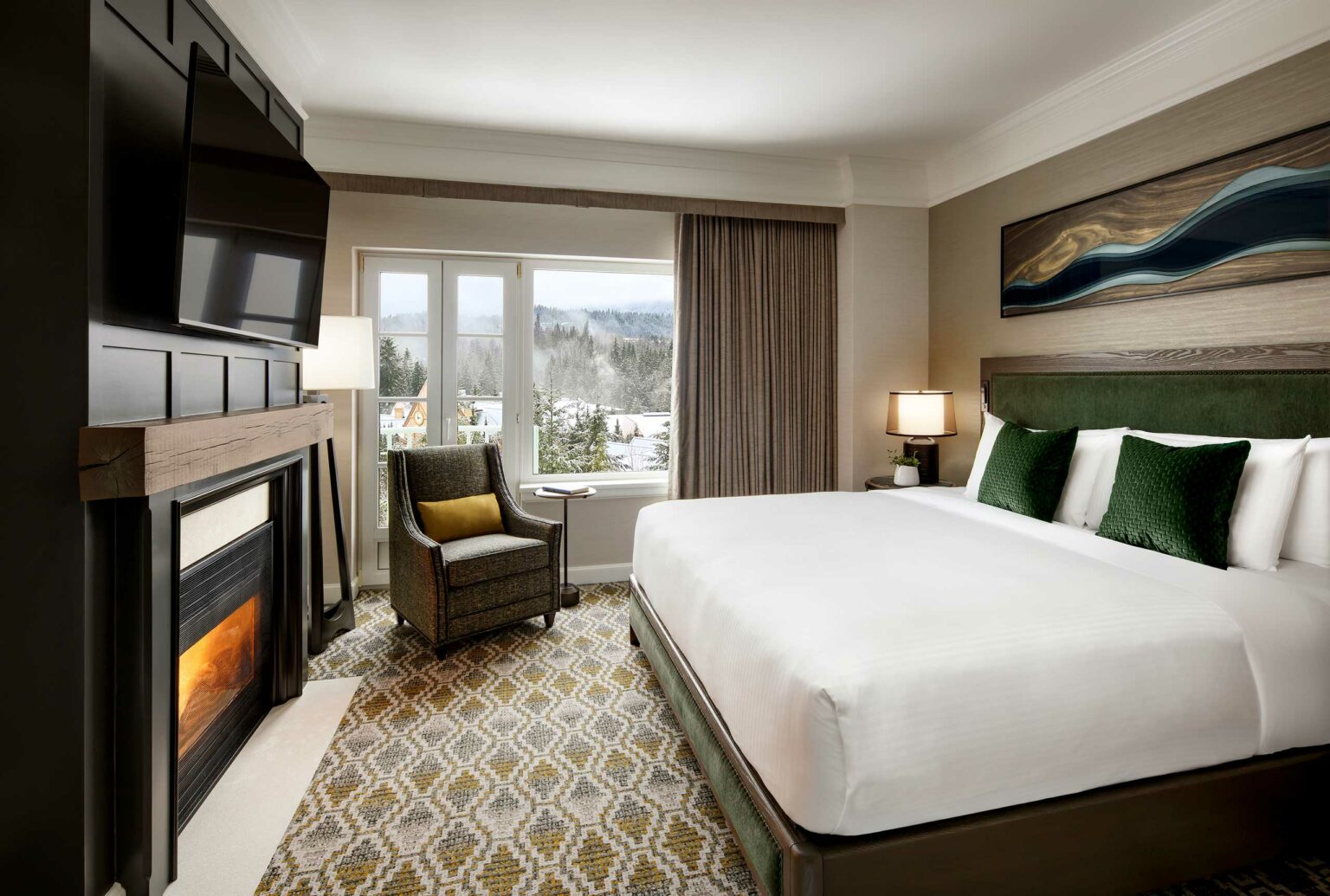Modern hotel room with a cozy fireplace, large bed, green pillows, and a scenic window view. Neutral tones and warm lighting create a relaxing atmosphere.
