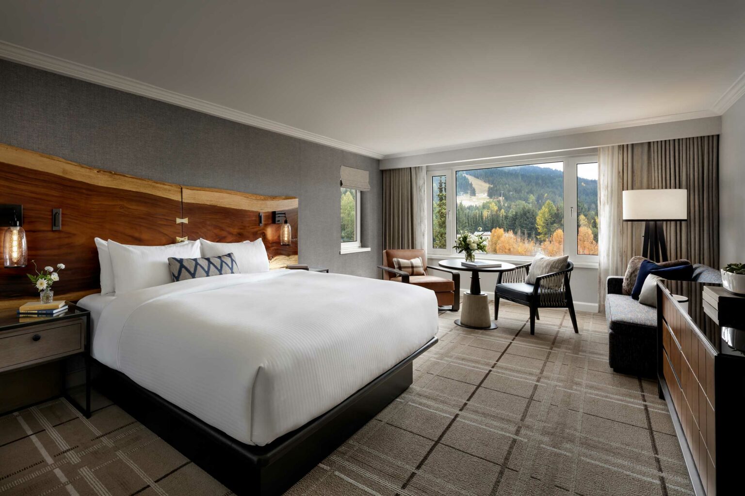 Luxurious hotel room with a large bed, wooden headboard, and elegant decor. A scenic window view of mountains adds a serene touch. Cozy and inviting ambiance.