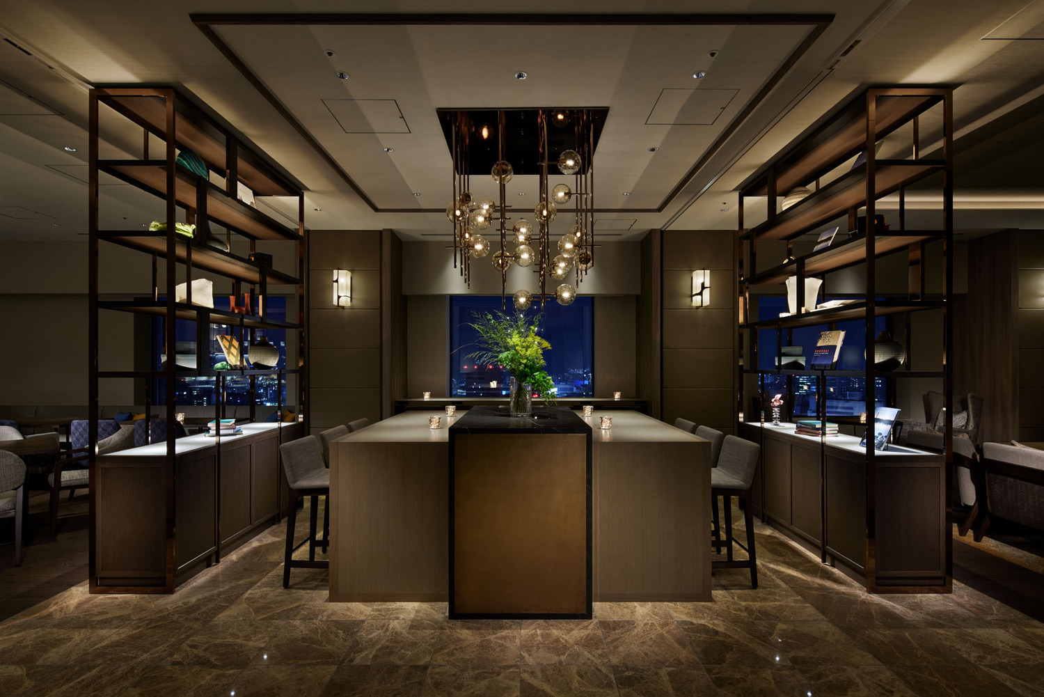 Elegant hotel lounge with dim lighting, featuring round tables, plush chairs, and a sleek bar in the background. The ambiance is cozy and sophisticated.