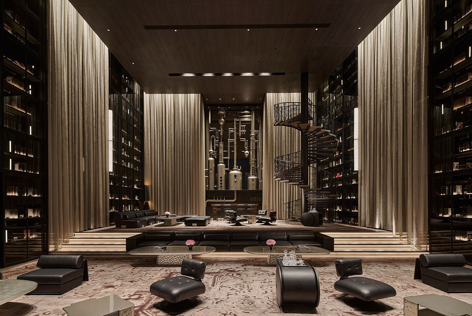 Luxurious lounge with sleek brown tones, featuring black leather seating, round tables, a spiral staircase, and an industrial backdrop. Warm, modern atmosphere.