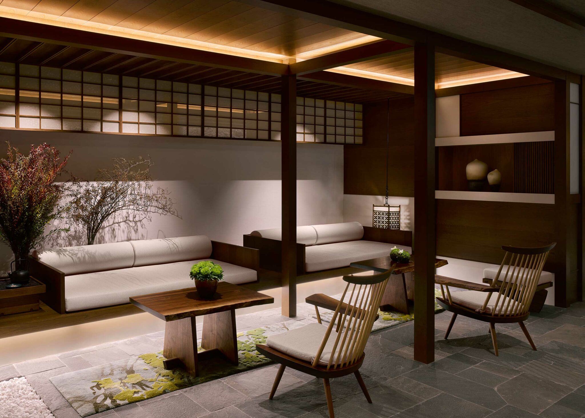 Modern Japanese-style hotel lounge with minimalistic decor. It features low white sofas, wooden chairs, tables, and soft warm lighting. Peaceful ambiance.