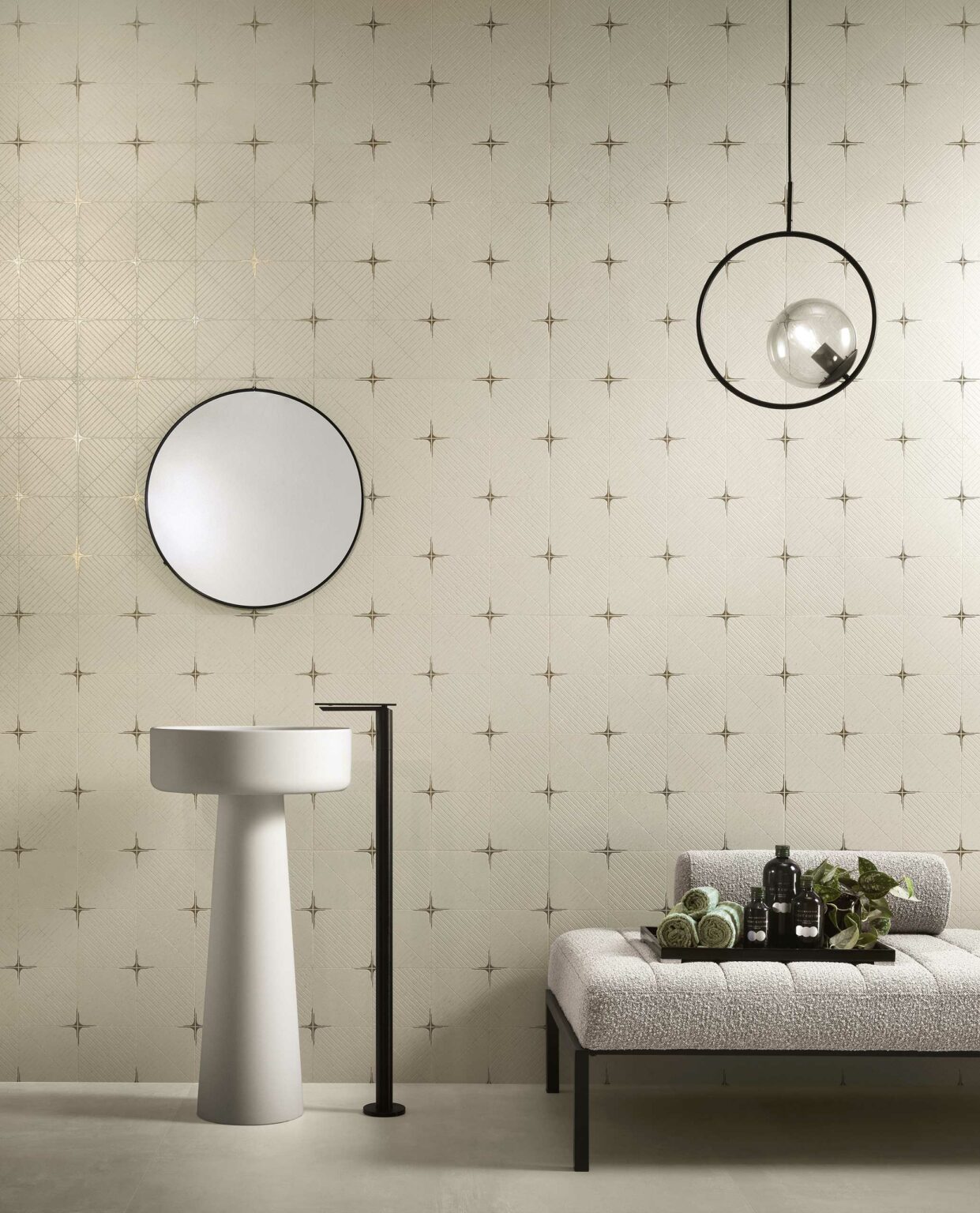Minimalist bathroom with star-patterned wall tiles. A round mirror above a sleek pedestal sink, modern lamp, and cushioned bench add elegance.