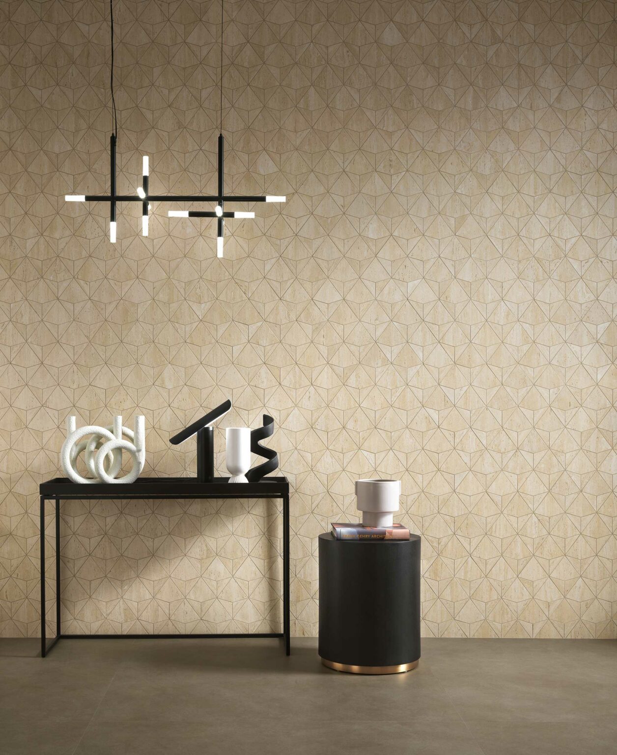 Modern interior with geometric beige tiled wall, black table with abstract sculptures, circular black side table, and crossed light fixture above.