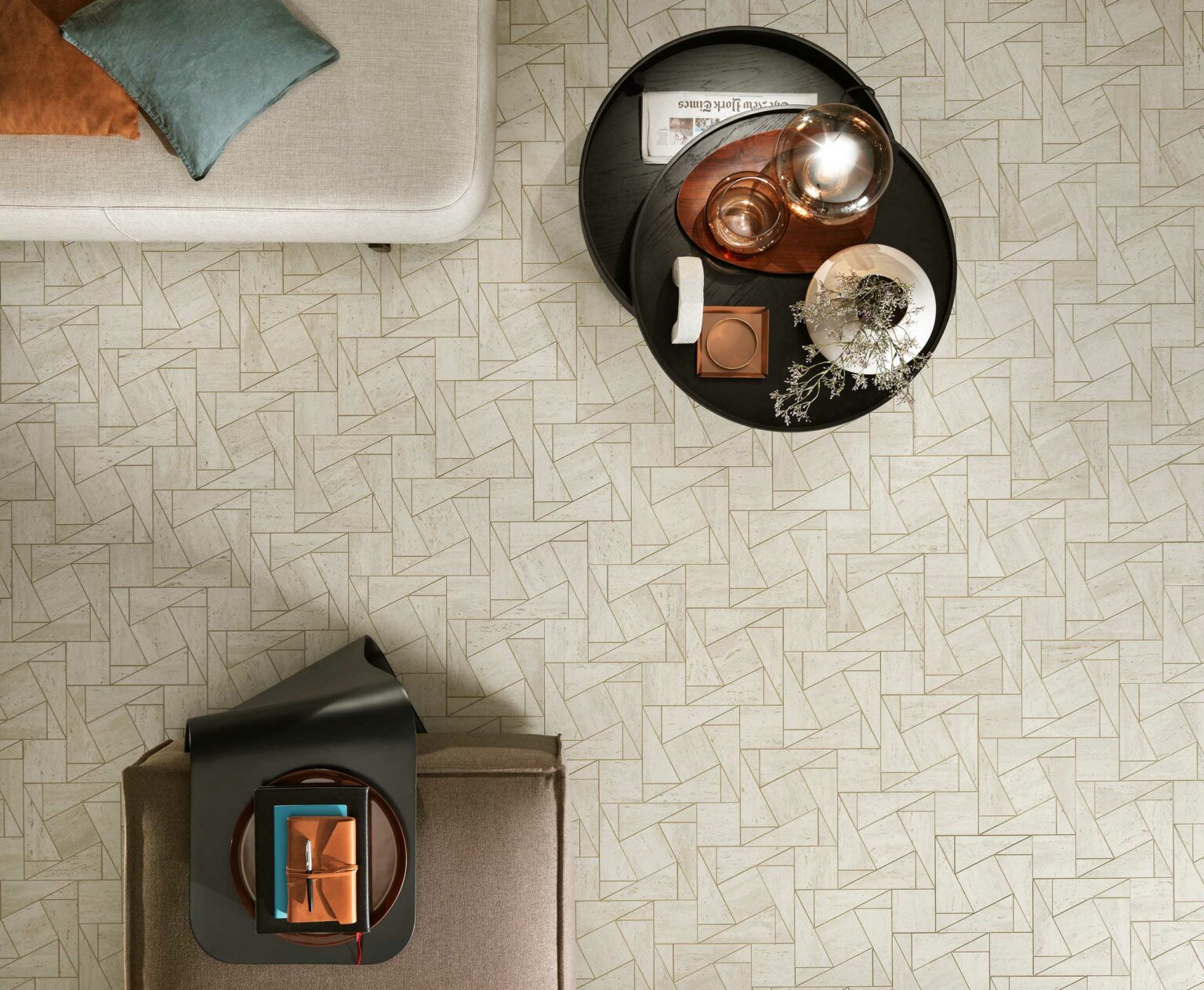 Overhead of a modern living room with geometric-patterned beige tile floor, a light sofa with teal and orange pillows, and a round black coffee table with decor items.