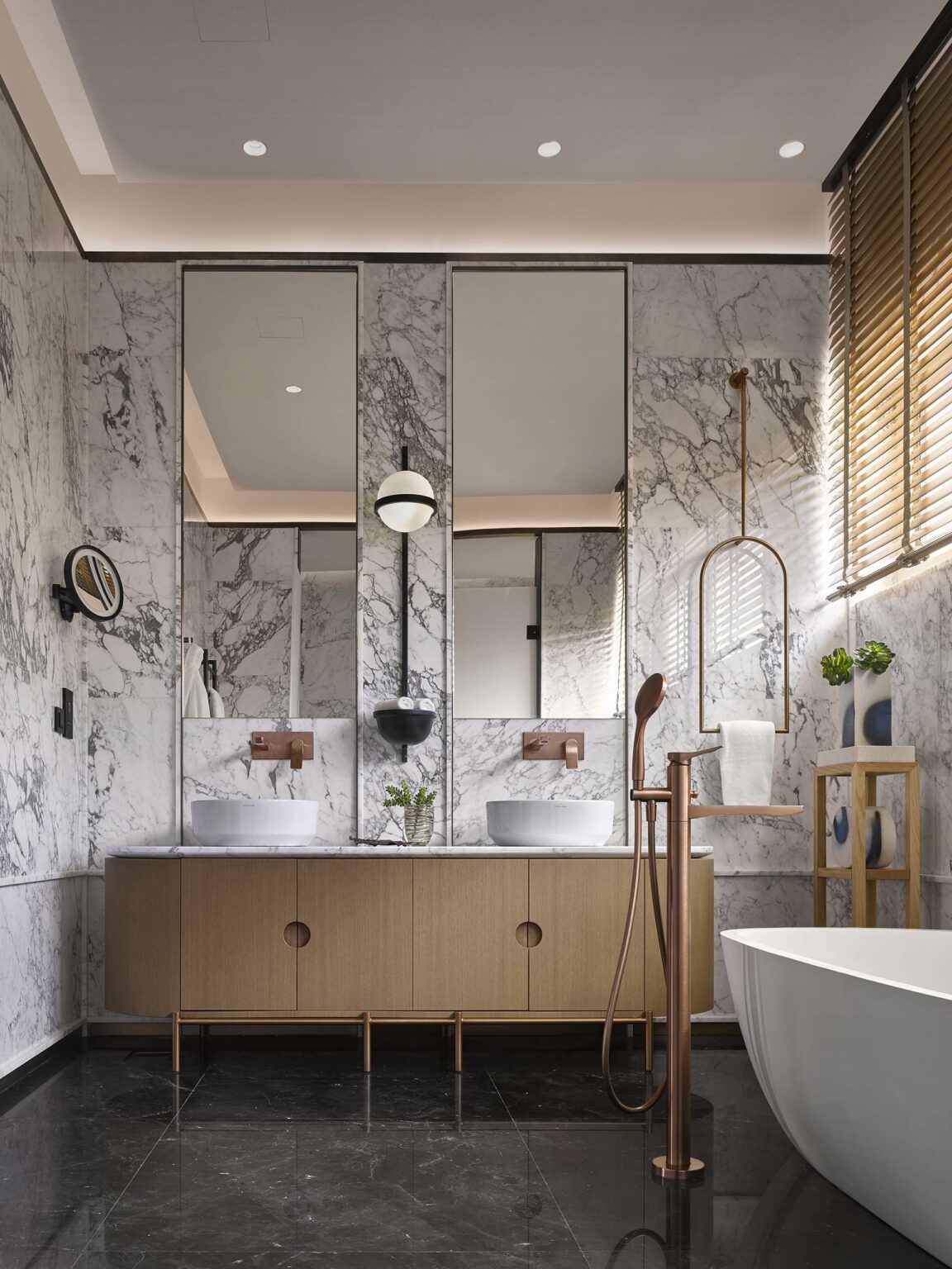 Elegant bathroom with marble walls and sleek lighting, featuring a double sink vanity with round basins, gold fixtures, and a modern freestanding tub.