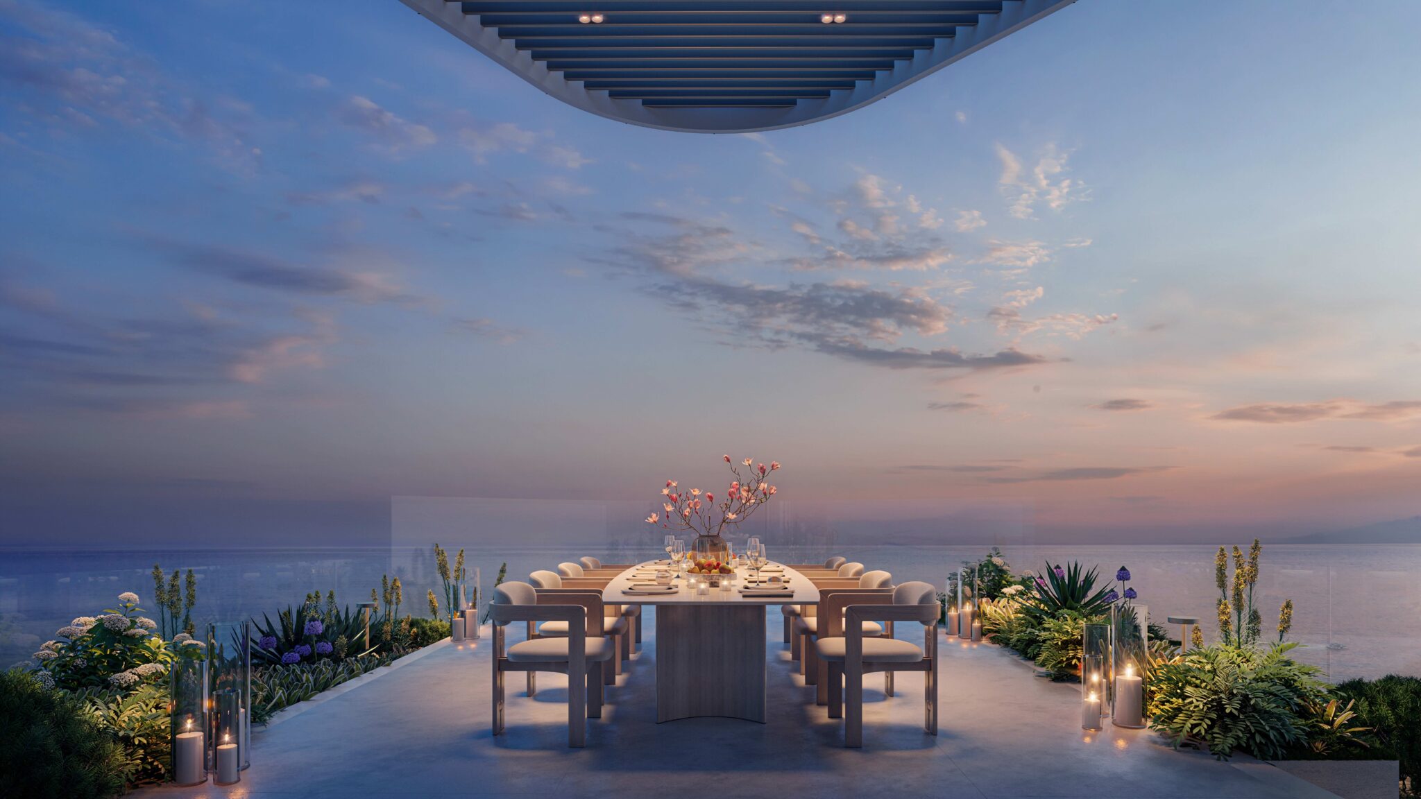 Elegant outdoor dining setup with a long table and chairs, surrounded by plants and candles, overlooking a serene ocean at sunset under a clear sky.