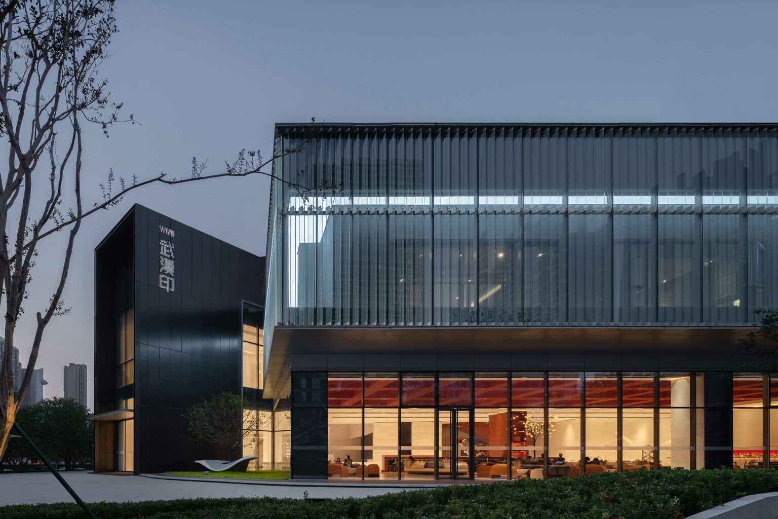 Chengtou Sunac Wuhan Emblem Sales Center exterior featuring a modern building at dusk with glass facade and illuminated interiors, showcasing a sleek, contemporary design.