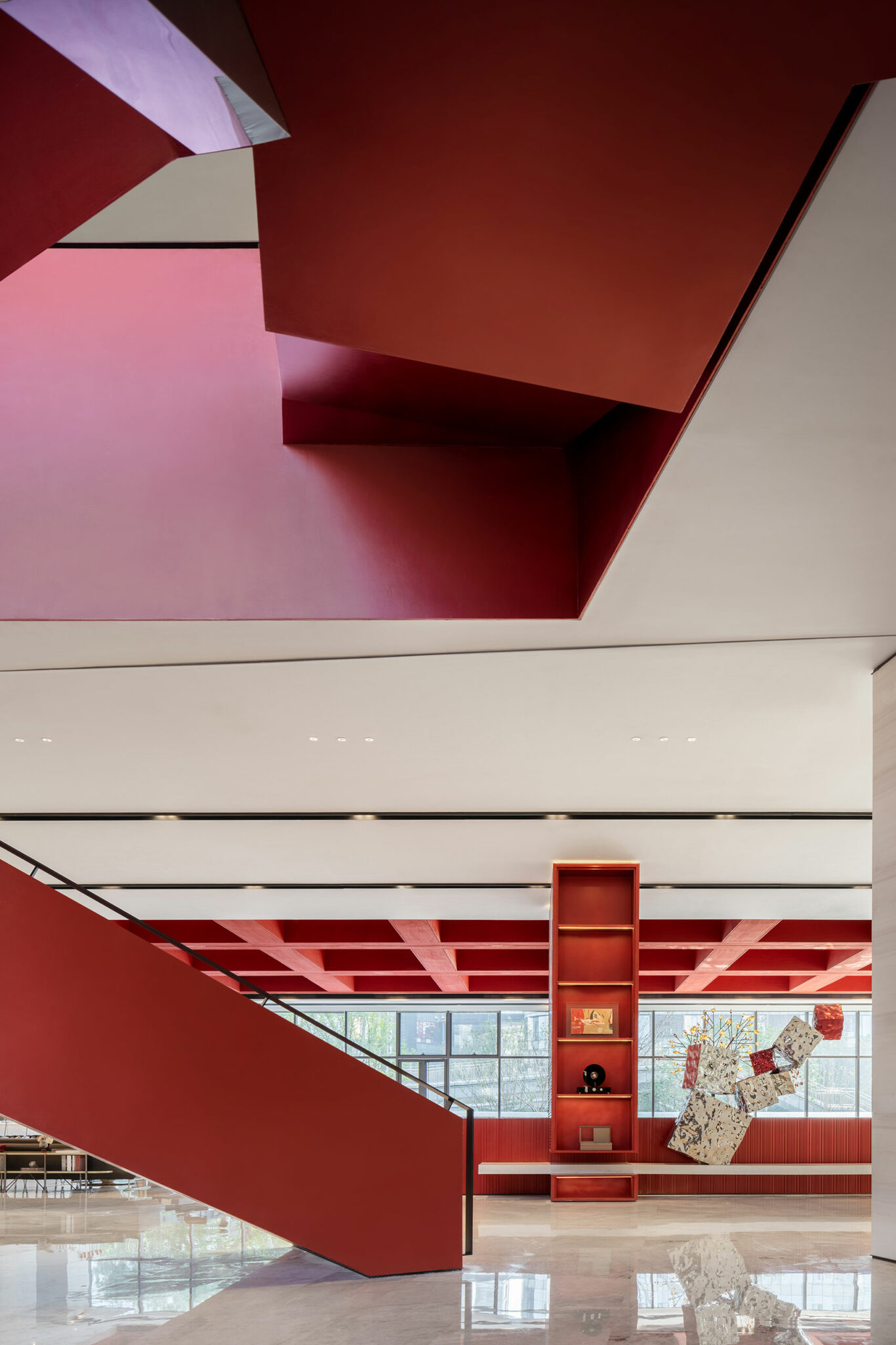 Spacious modern interior with bold red staircase and accents. Bright, open atmosphere with geometric shapes and a prominent wall display, exuding a stylish tone.