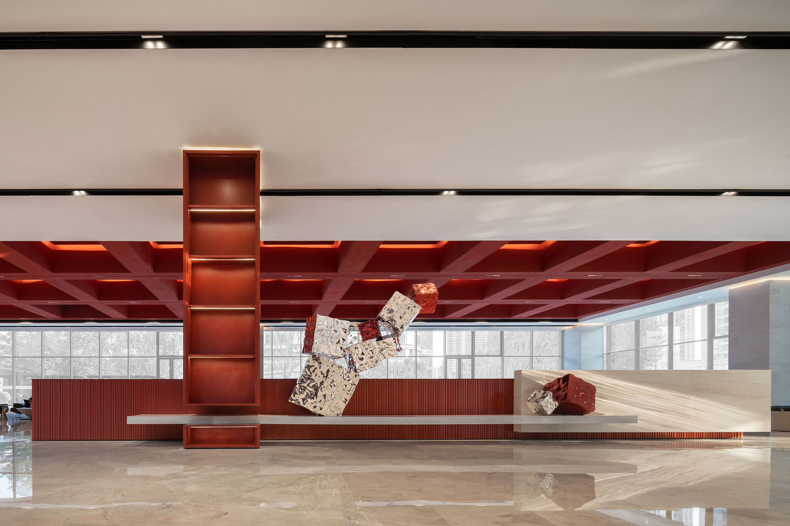 Modern lobby with geometric art installation. Red ceiling grid and shelving, marble floor, large windows. Minimalist and sophisticated ambiance.