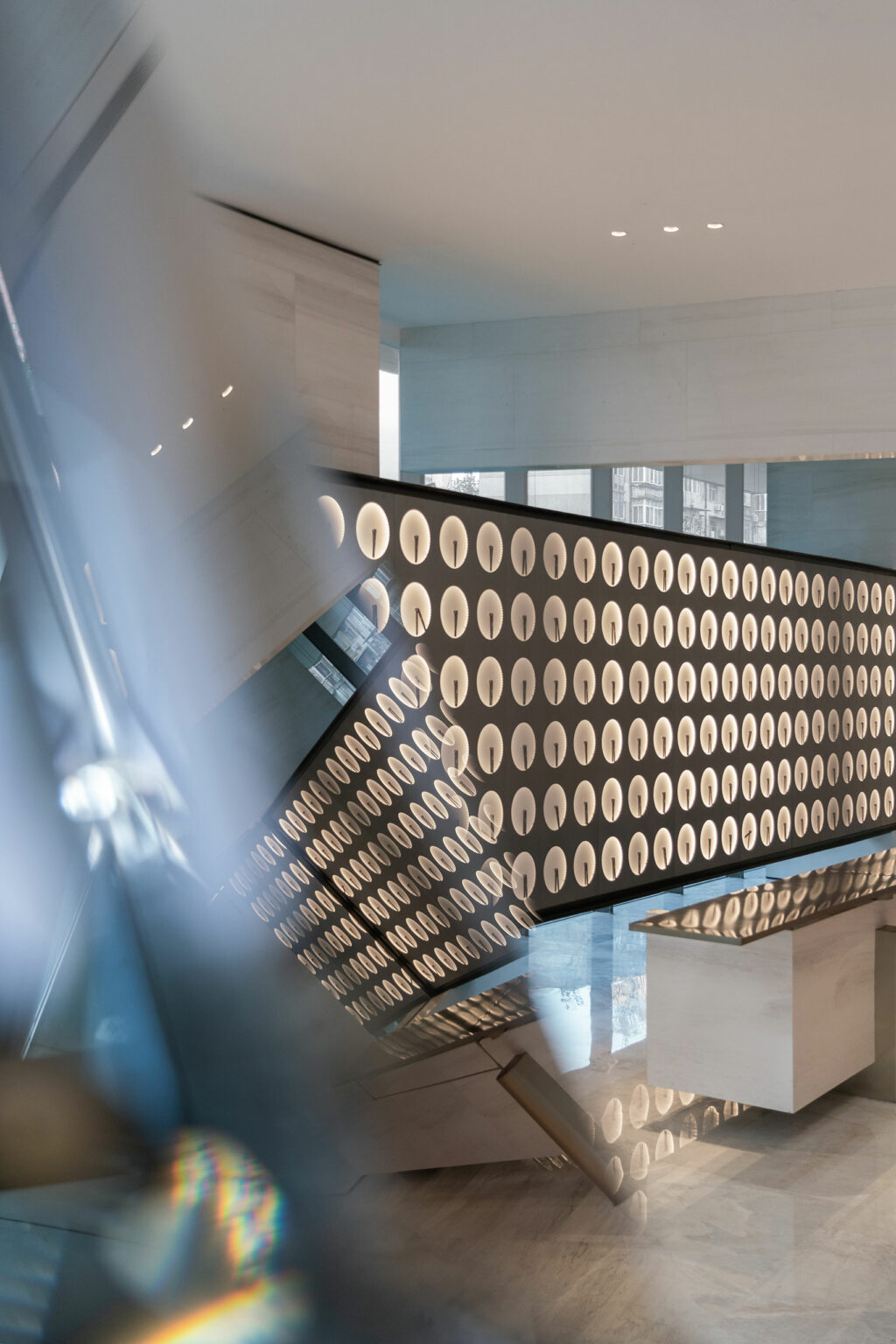 Futuristic interior with a curved, backlit wall featuring round cutouts. Soft lighting and sleek design create a modern, sophisticated ambiance.