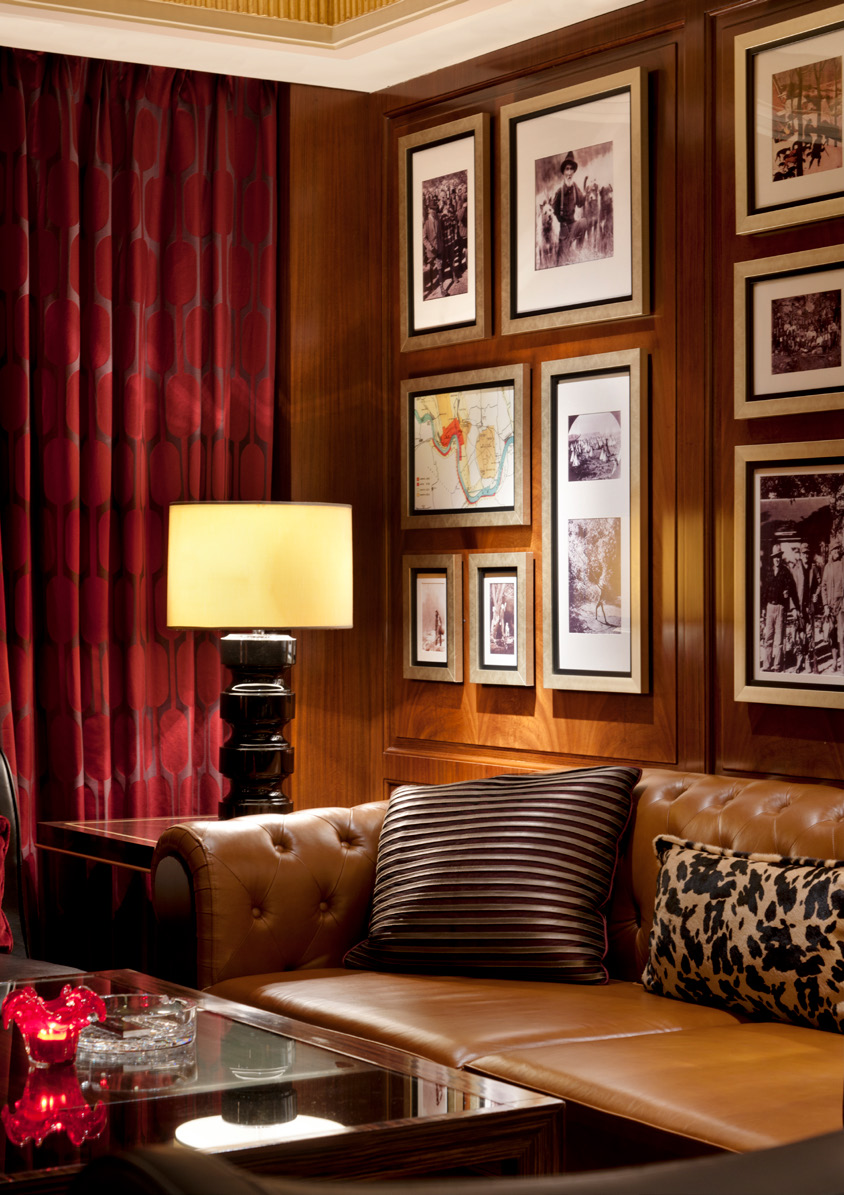 Elegant jazz bar lounge with a brown leather sofa, striped and patterned cushions, framed photos on wood-paneled walls, and a warm-lit lamp. Rich, cozy ambiance.