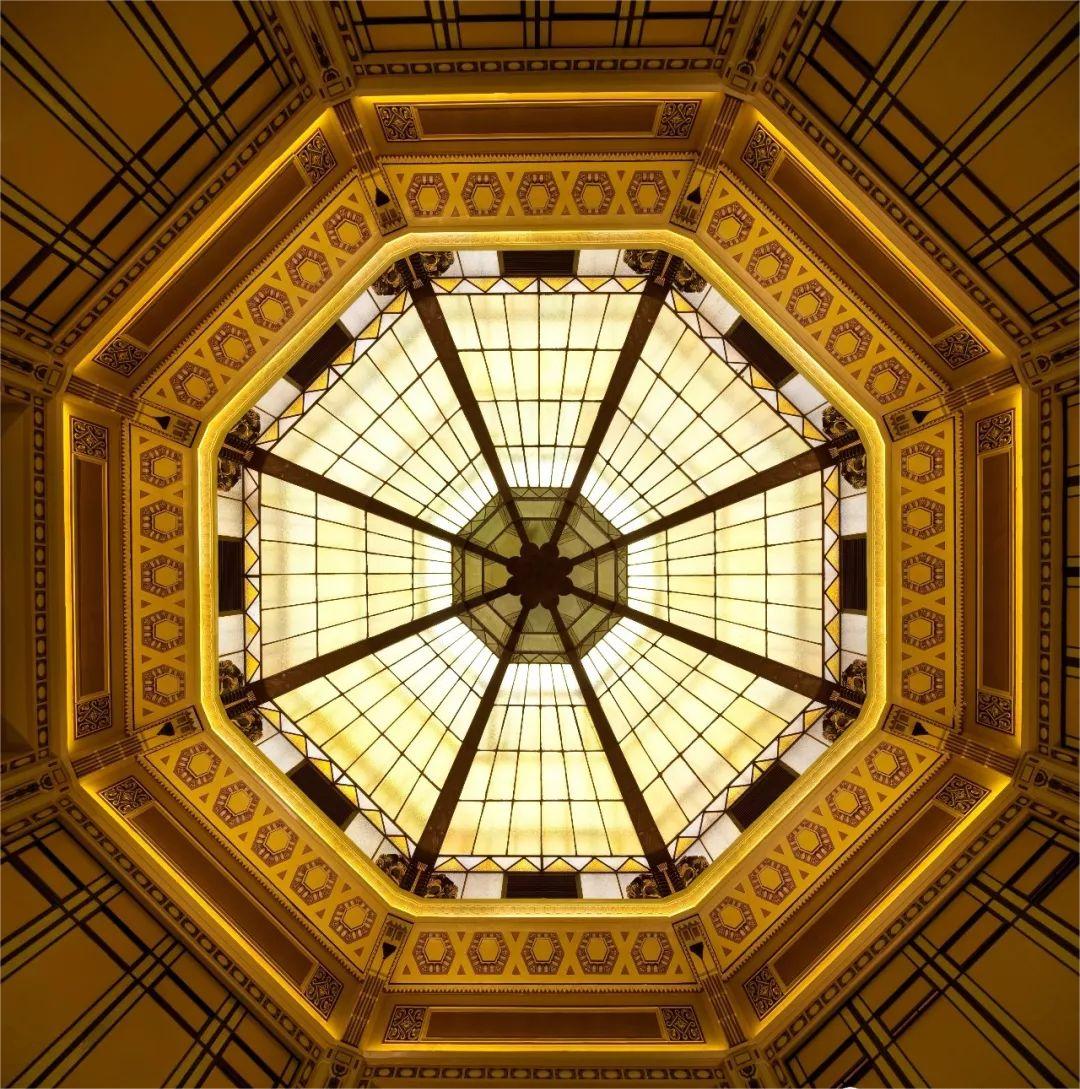 Octagonal stained glass ceiling with geometric patterns and warm yellow tones, creating an elegant and intricate design that radiates symmetry and balance.