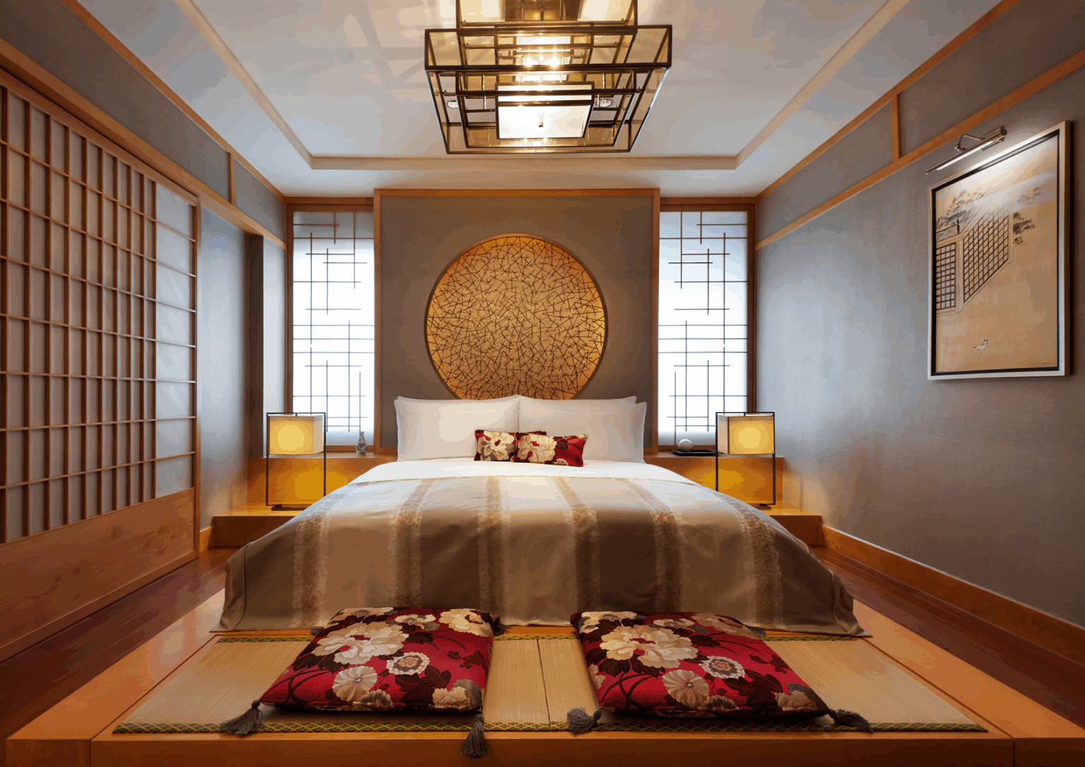 Modern suite bedroom with minimalist Japanese decor. Features a large bed with floral cushions, a circular wall art, shoji screens, and soft ambient lighting.