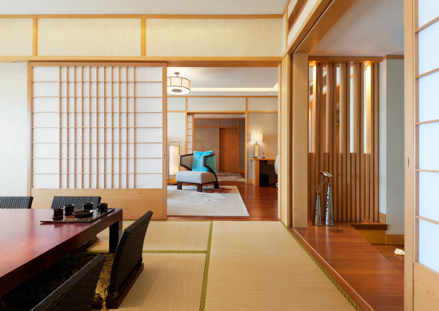 A serene Japanese-style room with tatami mats, a low wooden table, and sliding shoji doors. Wooden accents create a warm, minimalist atmosphere.