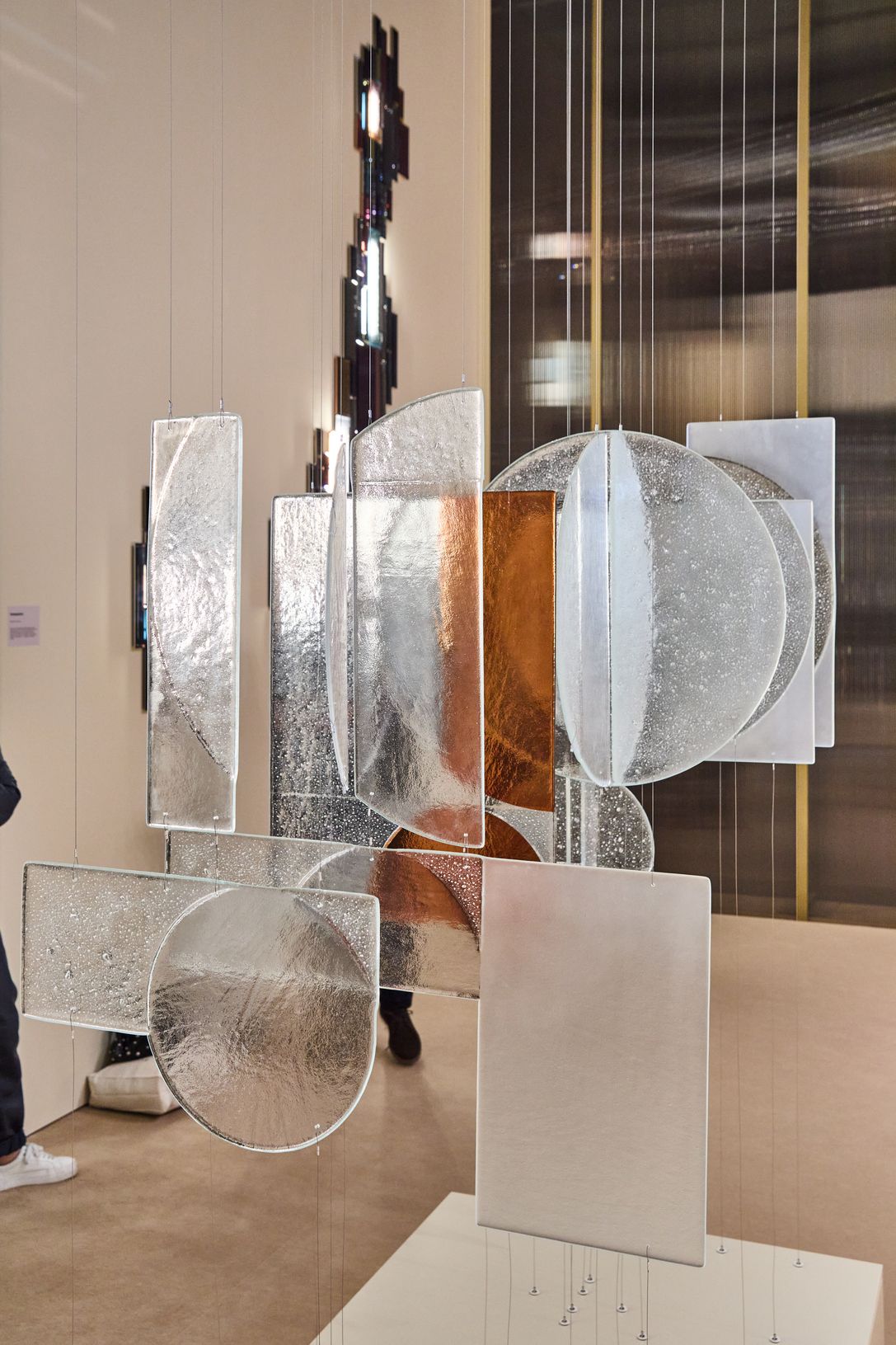 Hanging modern sculptures featuring rectangular and circular textured glass in silver and copper tones. Reflective surfaces and elegant lines create a sophisticated atmosphere.