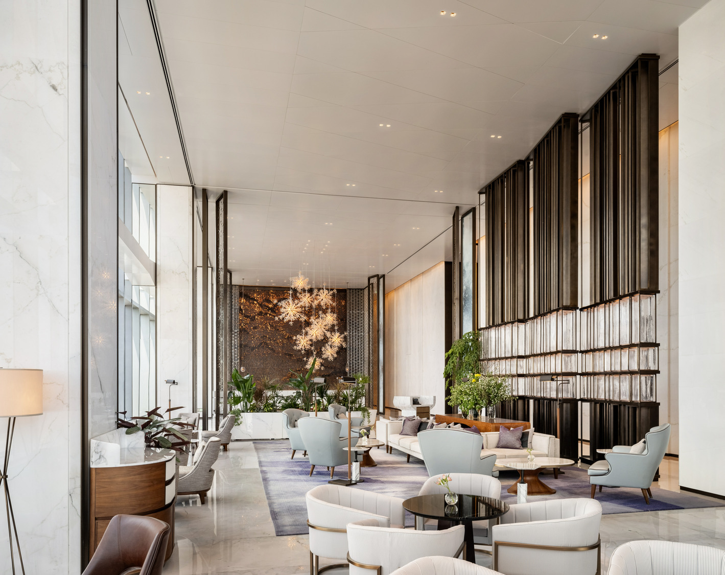 Luxurious hotel lobby with modern decor, featuring plush blue and white seating, marble floors, large wall art, and elegant chandeliers. A relaxing ambiance prevails.