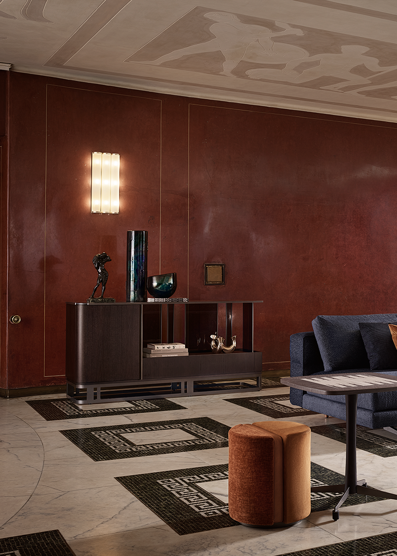 Luxurious living room with red walls, a sleek modern sideboard with dark wood finish, a navy sofa adorned with orange pillows and a throw, elegant lighting, and marble stairs. Sophisticated and warm.