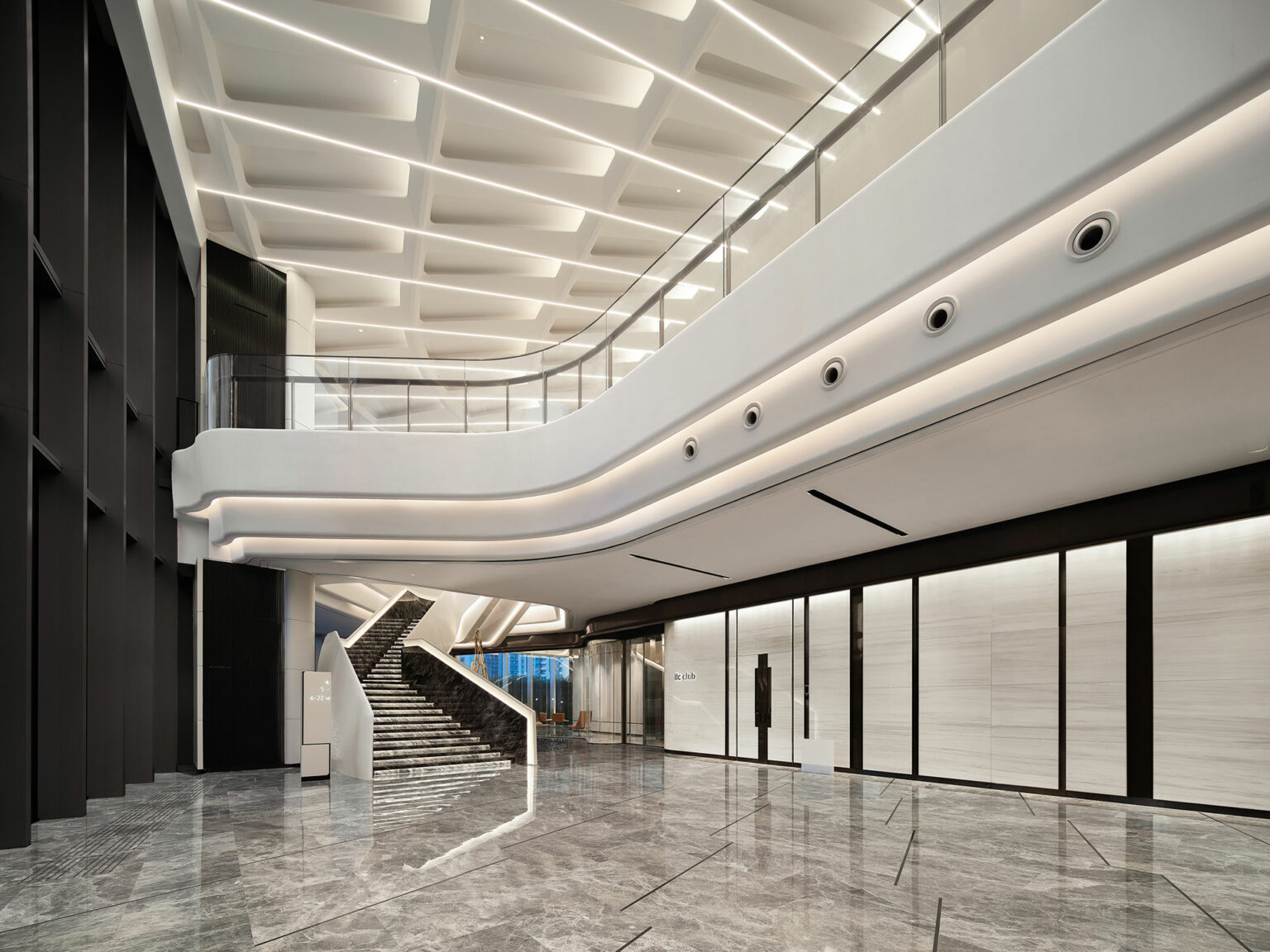 Modern, spacious office lobby with sleek marble floors and a grand staircase. Curved white ceiling and walls feature recessed lighting for an elegant, airy feel.