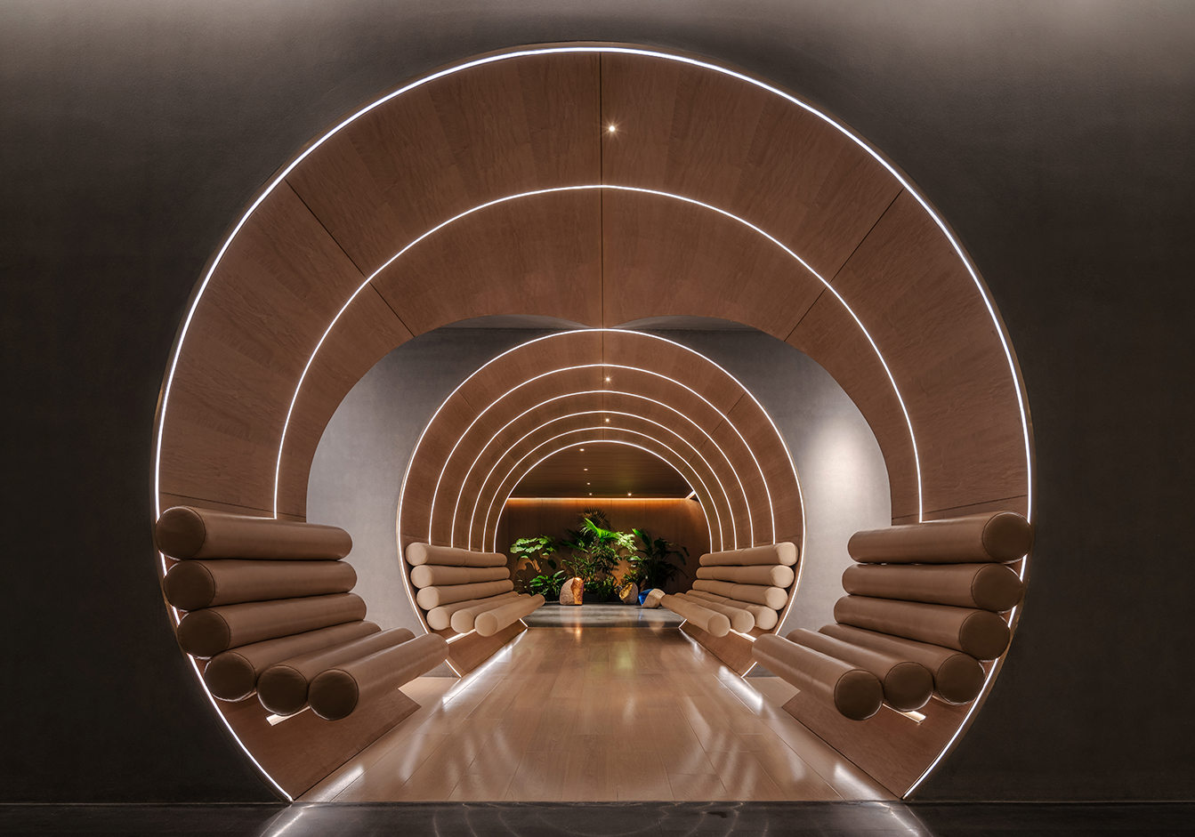 Futuristic tunnel view with circular wooden arches and glowing LED lines. Soft leather cylindrical seats are on either side, leading to lush green plants.