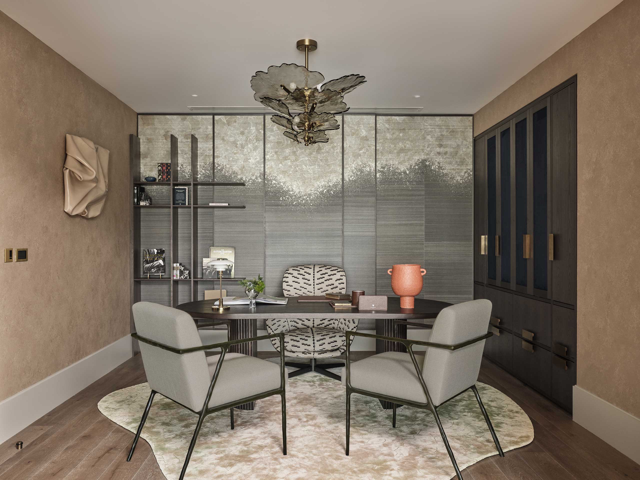 Elegant study with a round desk, two gray chairs, and a large vase. Textured wall panels and minimalist shelves create a modern ambiance.