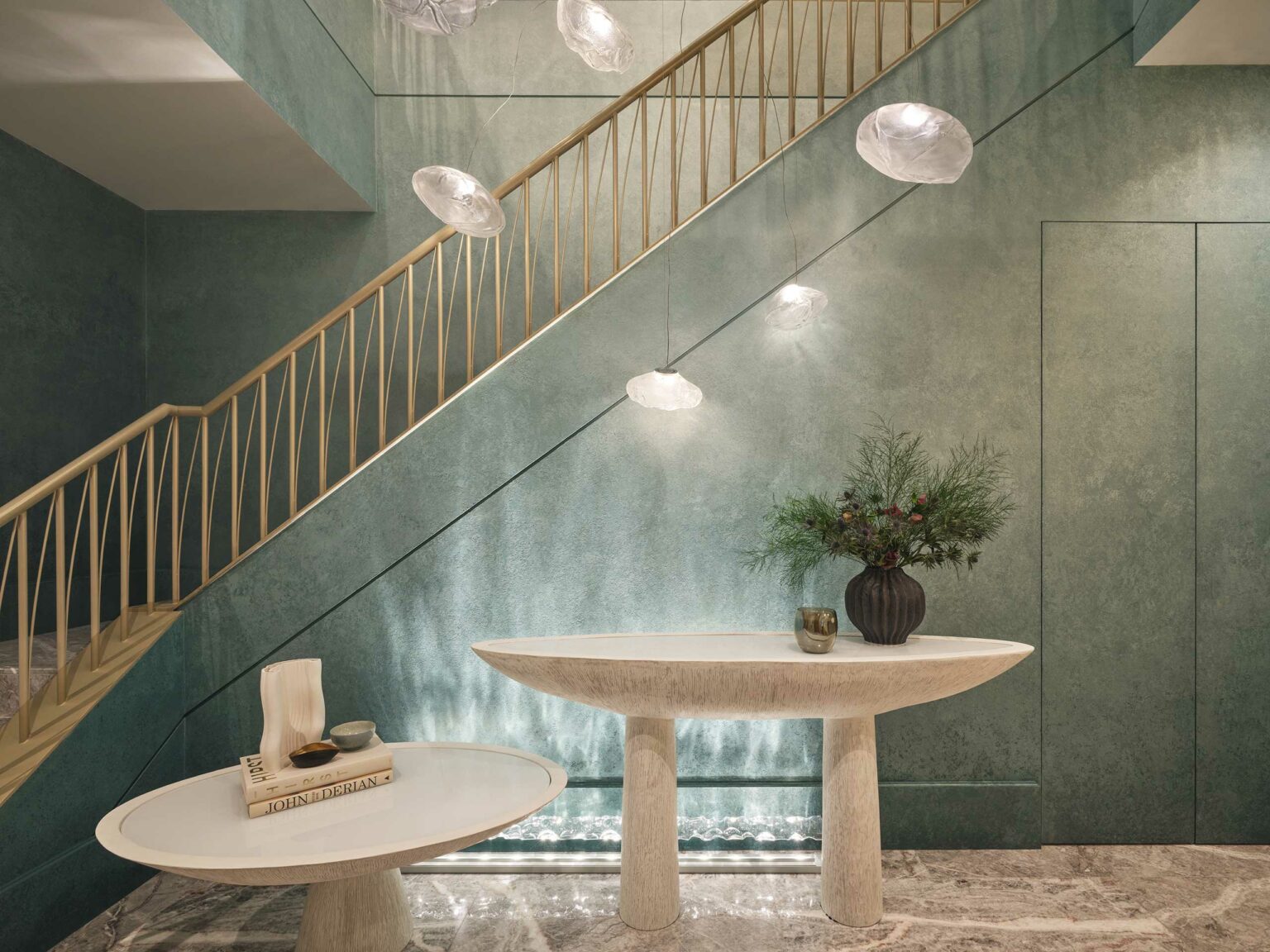 Modern interior with a stylish staircase, oval marble tables, and a black vase with greenery. Soft lighting creates a calm and elegant ambiance.