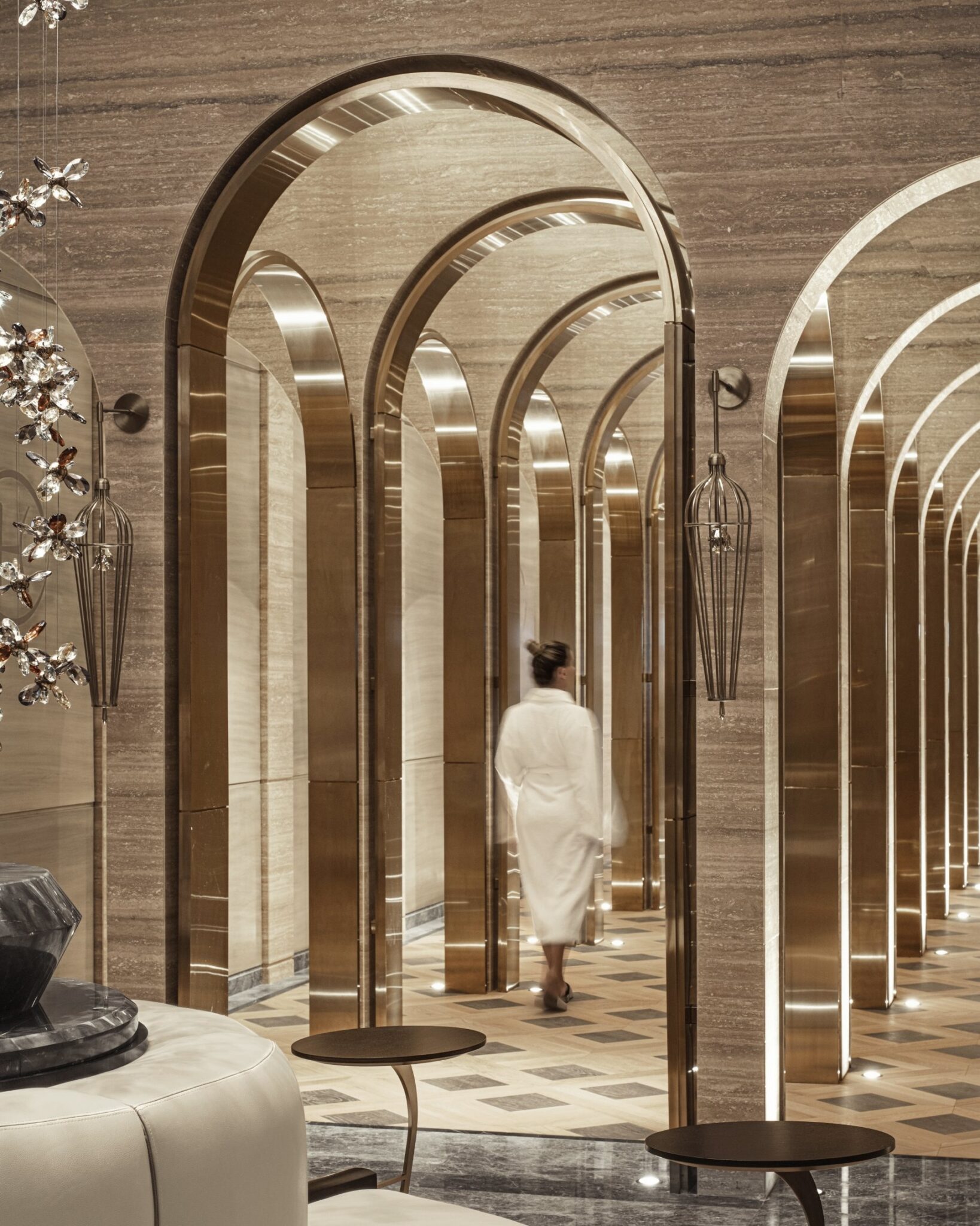 Luxurious resort spa interior with arched golden doorways and marble walls. A person in a white robe walks through the opulent, serene hallway.