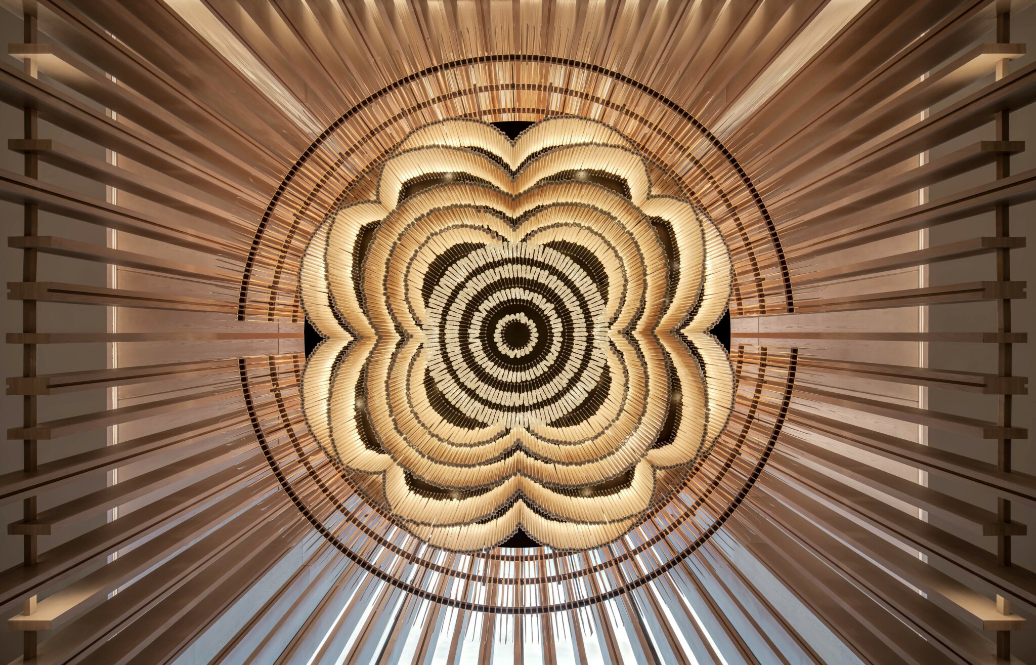 Abstract wooden ceiling design viewed from below, resembling a concentric flower pattern. Warm tones and radial symmetry create a serene, artistic ambiance.
