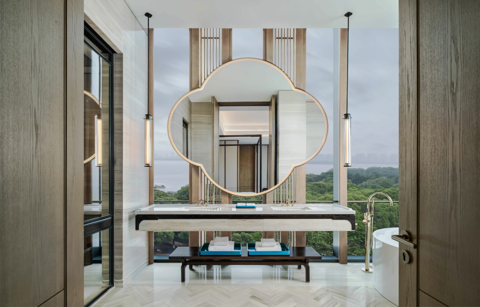 Luxurious suite bathroom with a large decorative mirror, pendant lights, and a marble countertop. A soaking tub and a scenic window view create a serene ambiance.