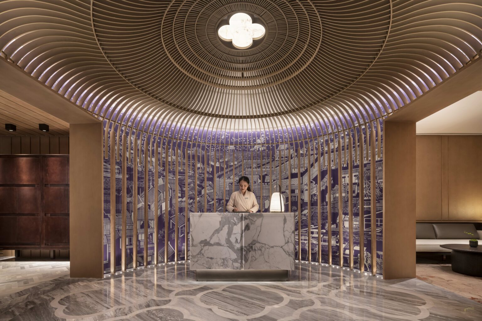 Luxurious hotel spa lobby with a marble reception desk. A receptionist stands beneath a dome-like ceiling with wooden slats and intricate wall art. Warm lighting sets a serene tone.