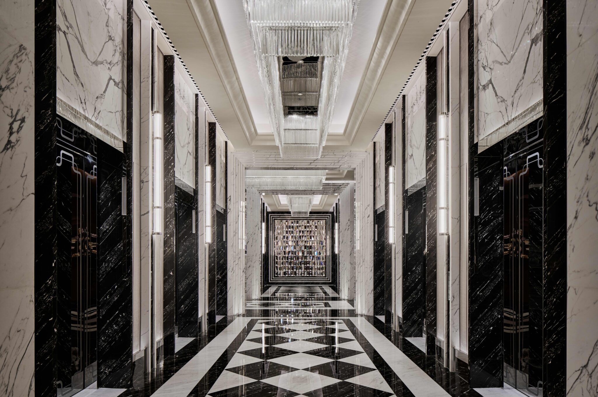 Luxurious hotel lift lobby with black and white marble walls and floor, featuring geometric patterns. Elegant chandeliers enhance the opulent, sophisticated atmosphere.