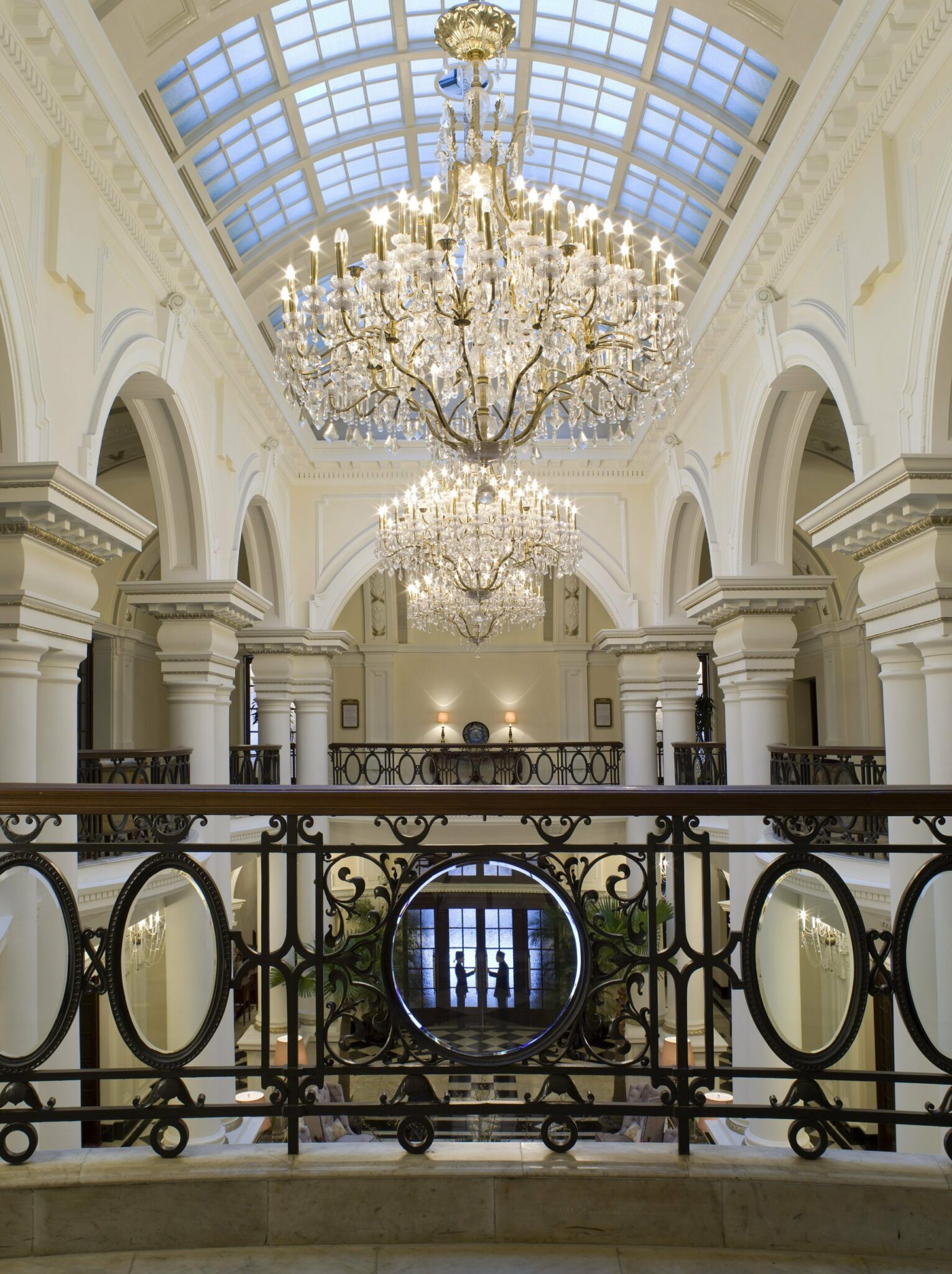 Elegant interior with grand chandeliers, arched ceilings, and ornate iron railing. Soft ambient light creates a luxurious and majestic feel.