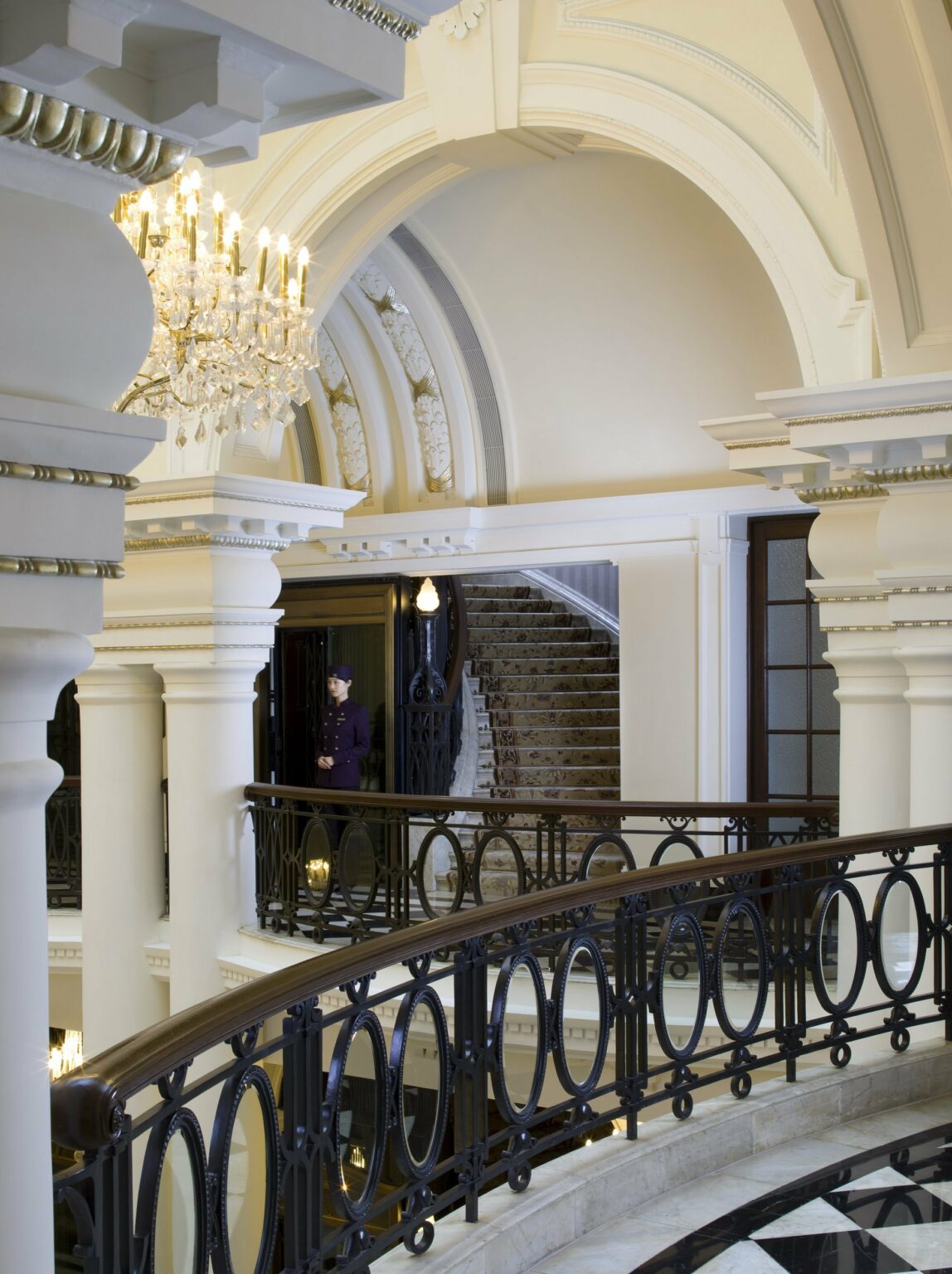 Elegant interior featuring an ornate chandelier, arched ceilings, and a sweeping staircase, framed by decorative railings.
