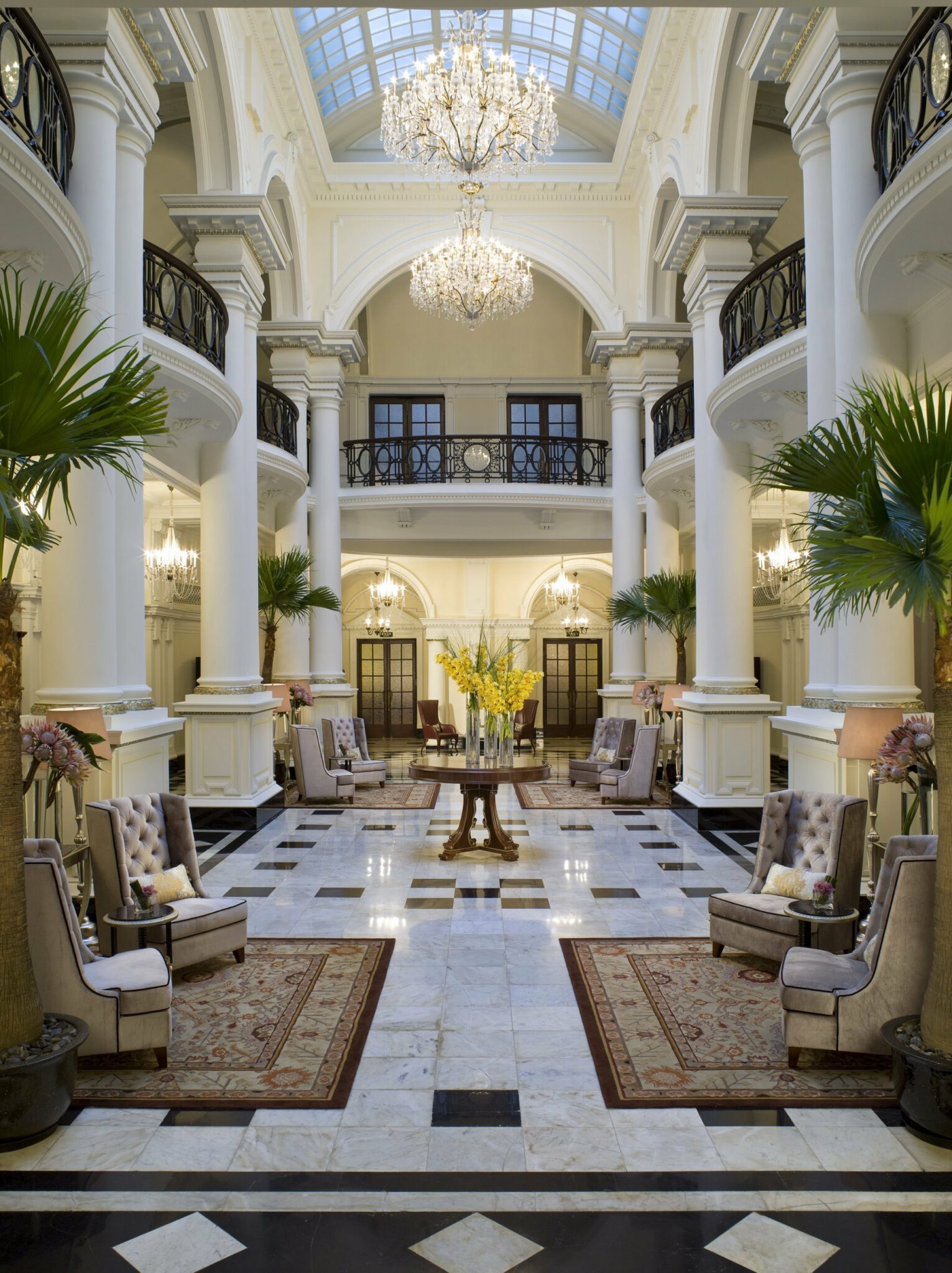 Elegant lobby interior featuring an ornate chandelier, arched ceilings, plush armchairs, and marbled flooring.
