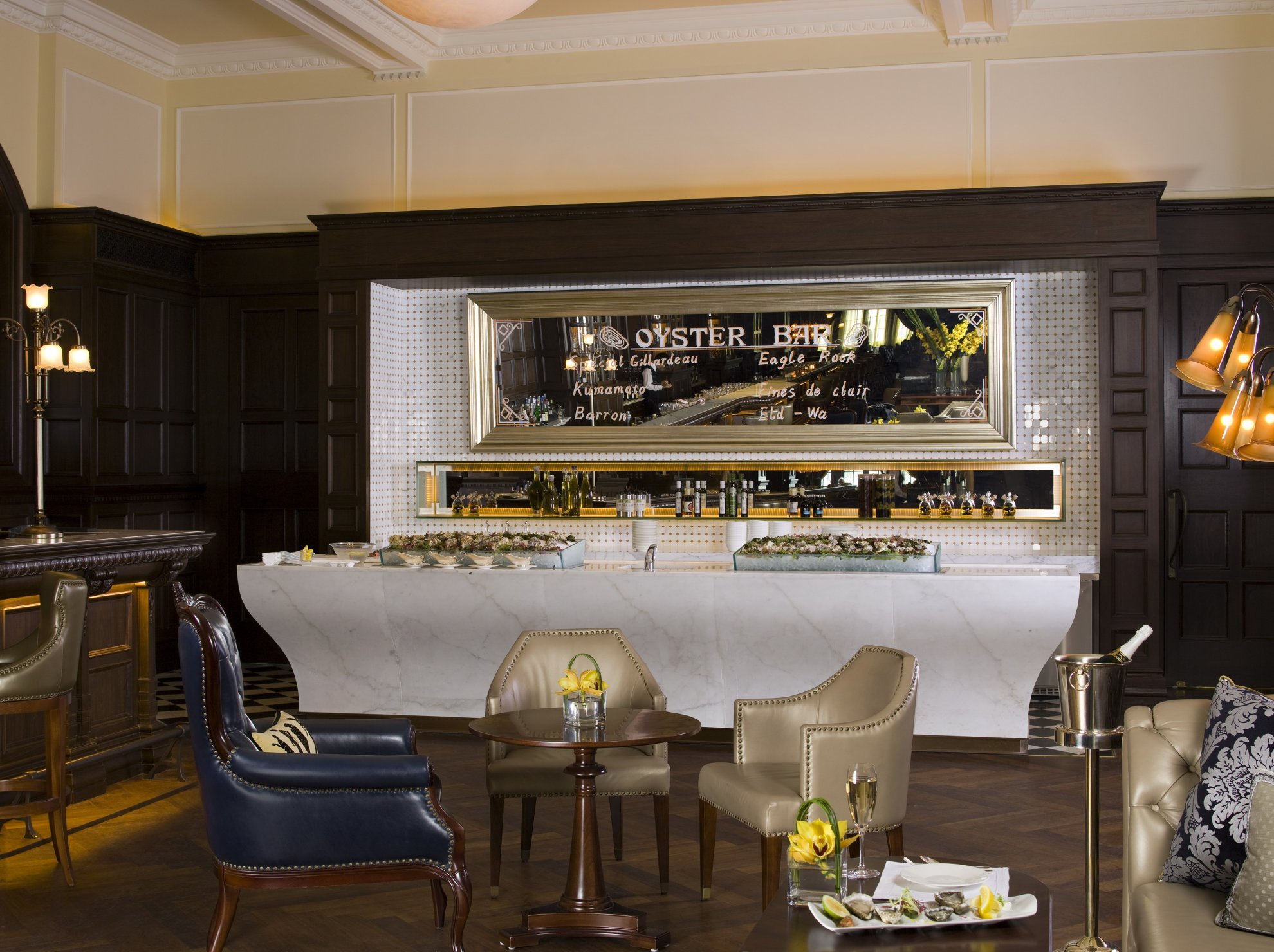 An elegant oyster bar featuring a marble counter, a decorative mirror, and a selection of fresh oysters displayed, surrounded by classic seating, creating a refined dining atmosphere.