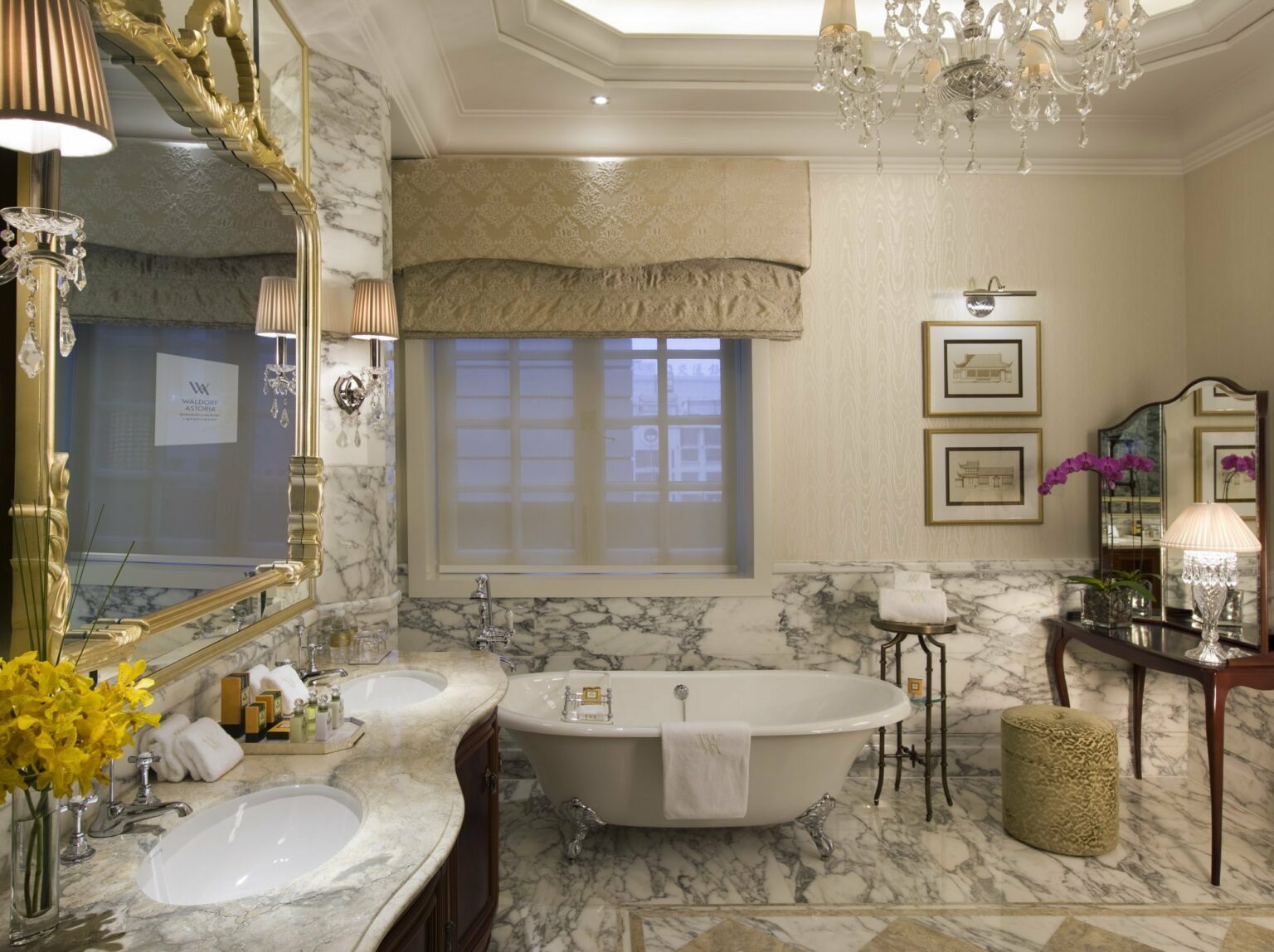 Luxurious bathroom featuring marble walls, a freestanding bathtub, elegant lighting, and decorative details including flowers and artwork.