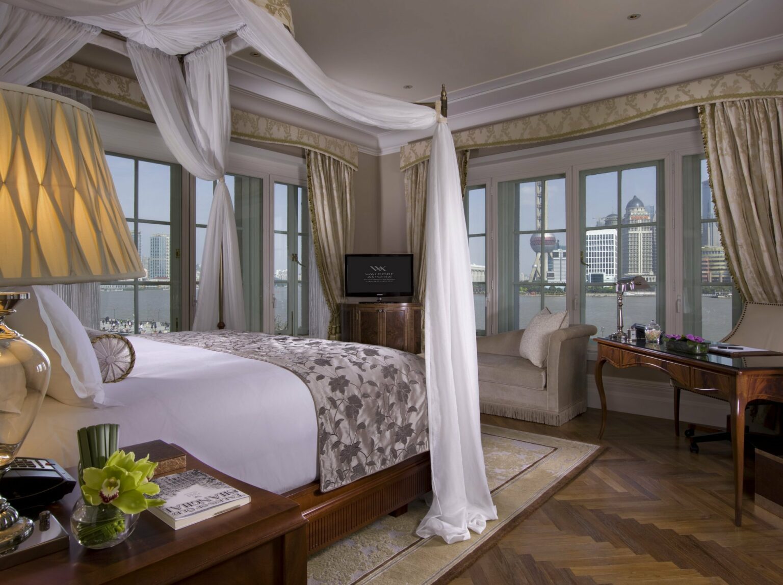 Luxurious bedroom with a four-poster bed, elegant decor, and sweeping views of the Shanghai skyline through large windows.