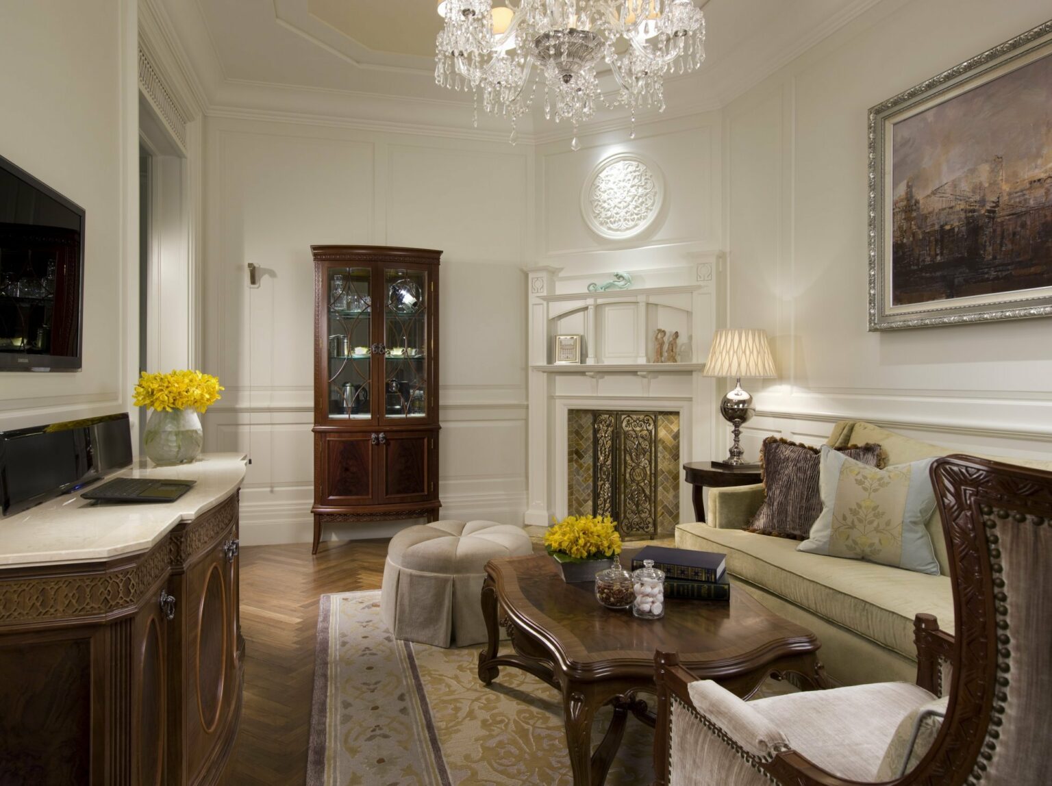 Elegant suite living room featuring a chandelier, vintage furniture, a glass-front cabinet, and yellow flower arrangements.