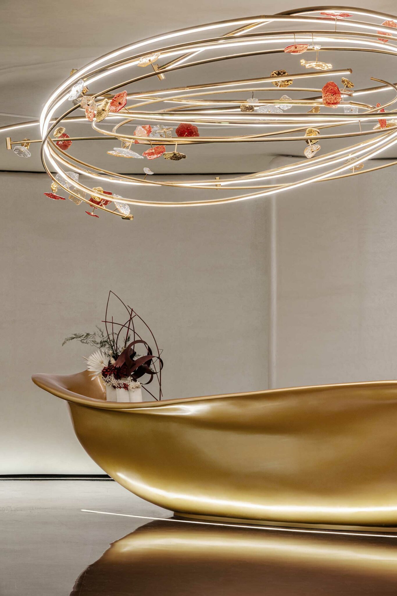 A sleek modern interior with a golden, curved reception desk against a minimalist backdrop. Above, an artistic, spiral light fixture adds elegance.