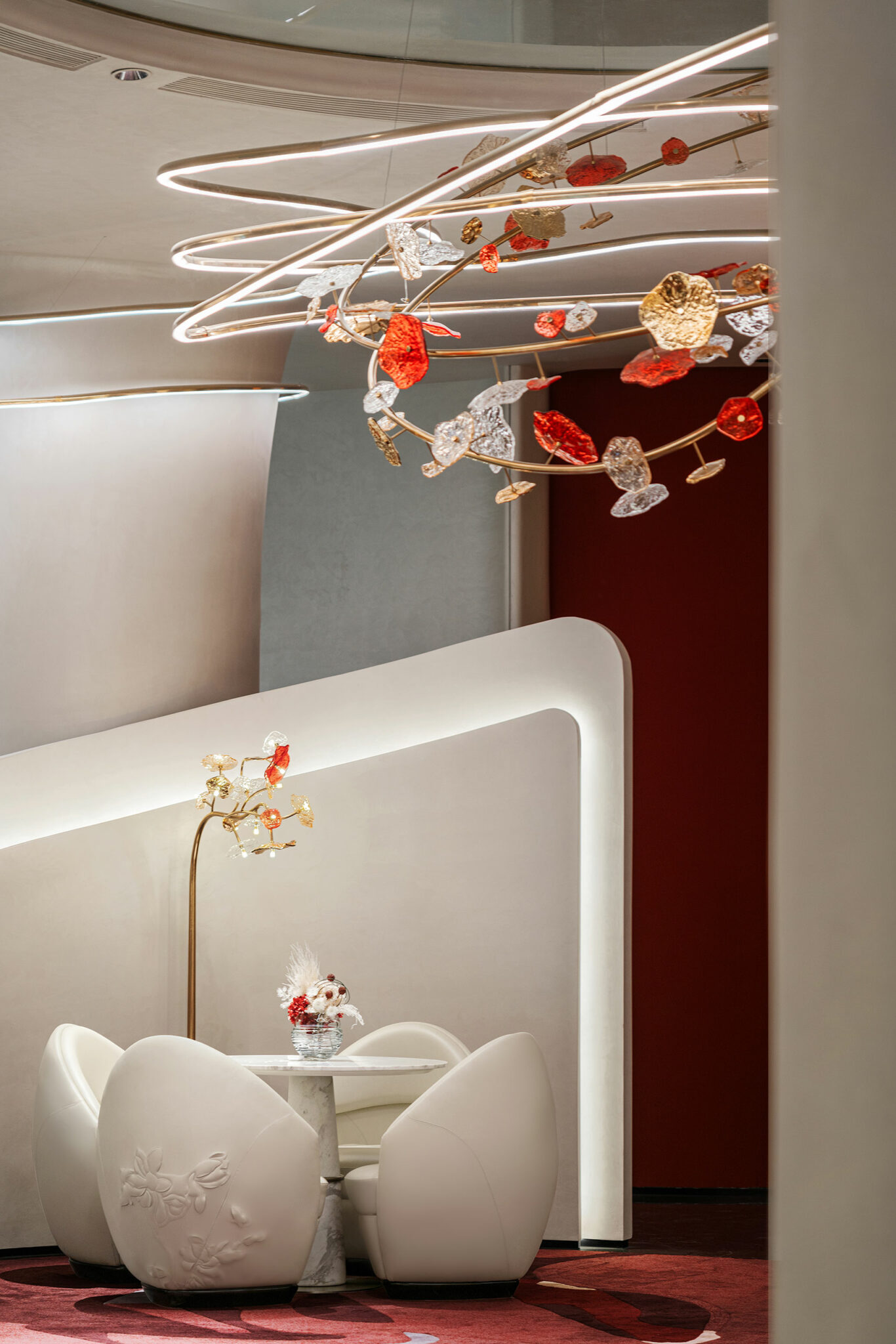 Elegant interior with modern white chairs and table set against curvy walls. A decorative ceiling light with red and gold accents adds a luxurious touch.