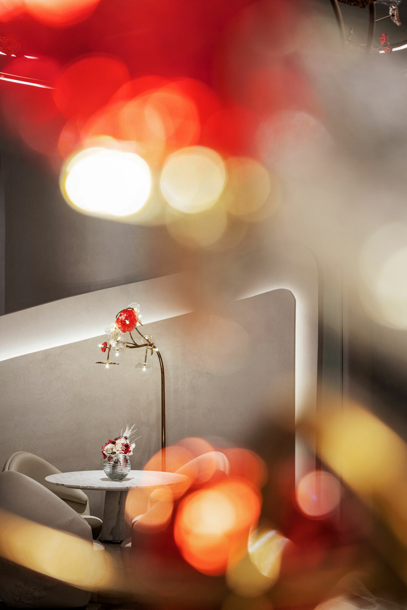 Cozy seating area with a small round table, floral centerpiece, and elegant lamp. Foreground has abstract red and gold bokeh lights, creating a warm ambiance.