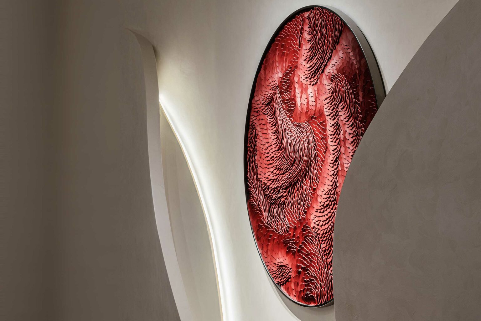 Abstract red artwork with swirling, textured patterns, mounted on a white wall with smooth curves. The scene feels dynamic and modern.